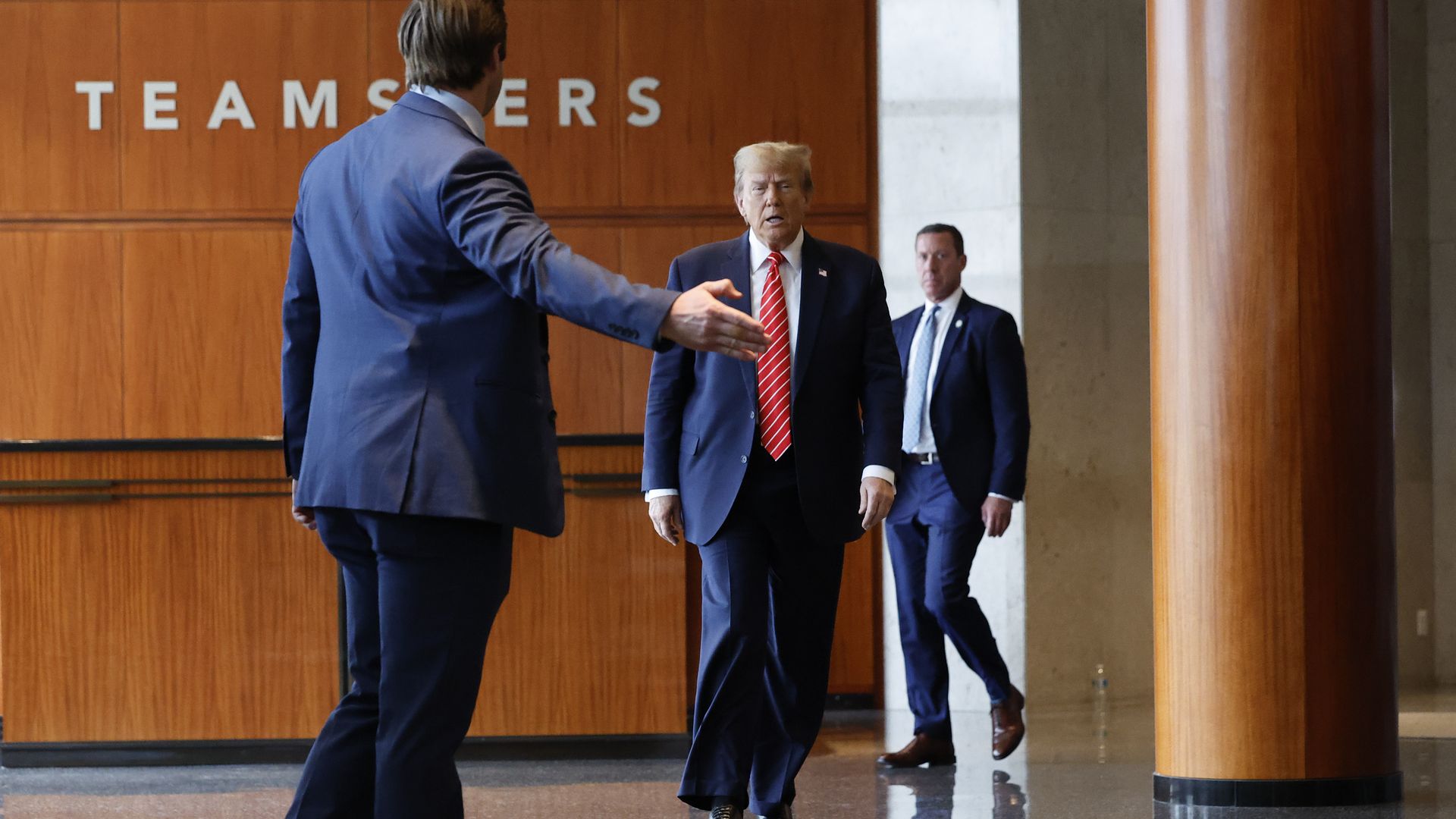 Donald Trump walks in a building with a Teamsters sign on a wall behind him.