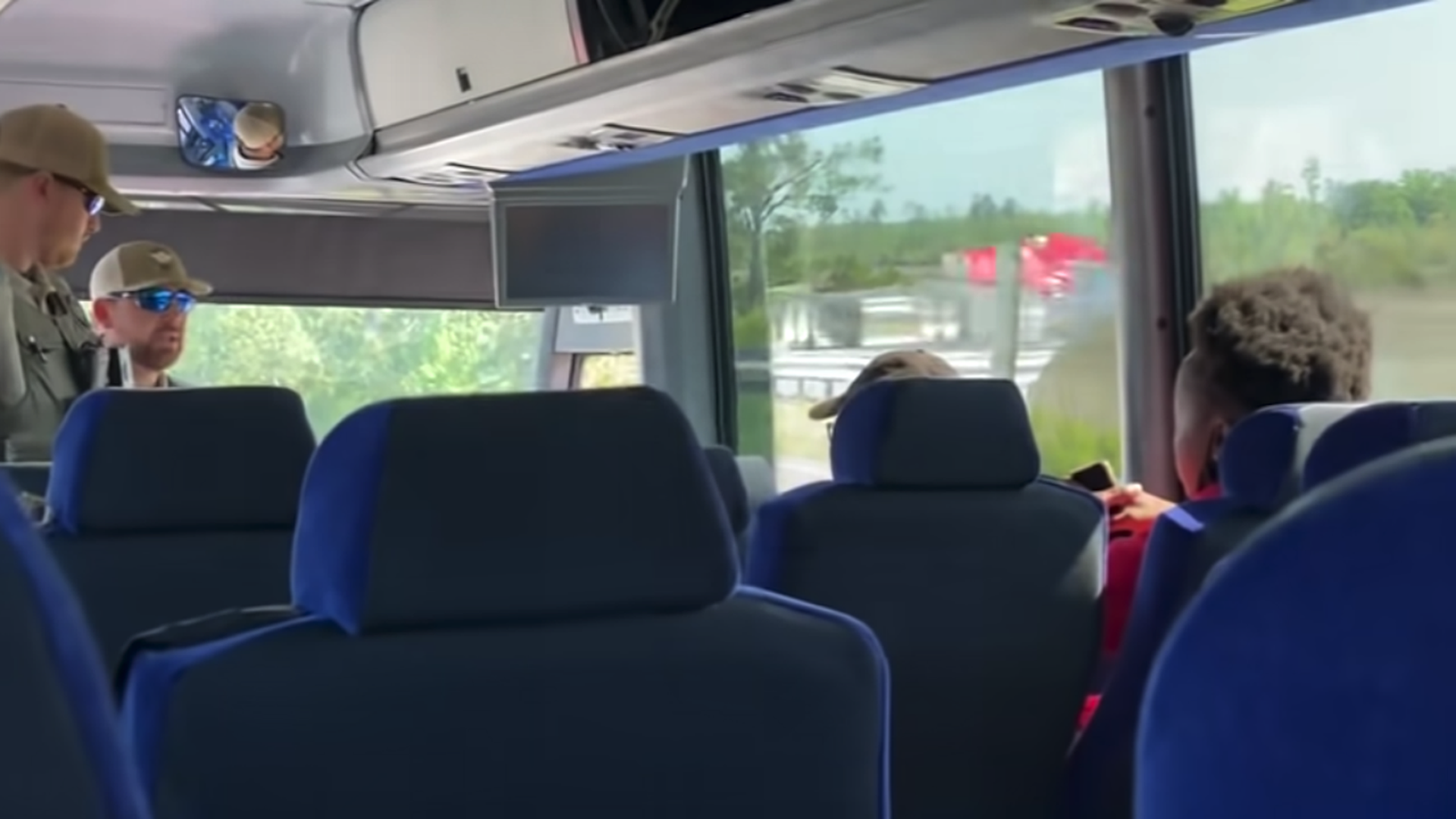 A screenshot of a YouTube video with a law enforcement officer addressing a team on a bus.