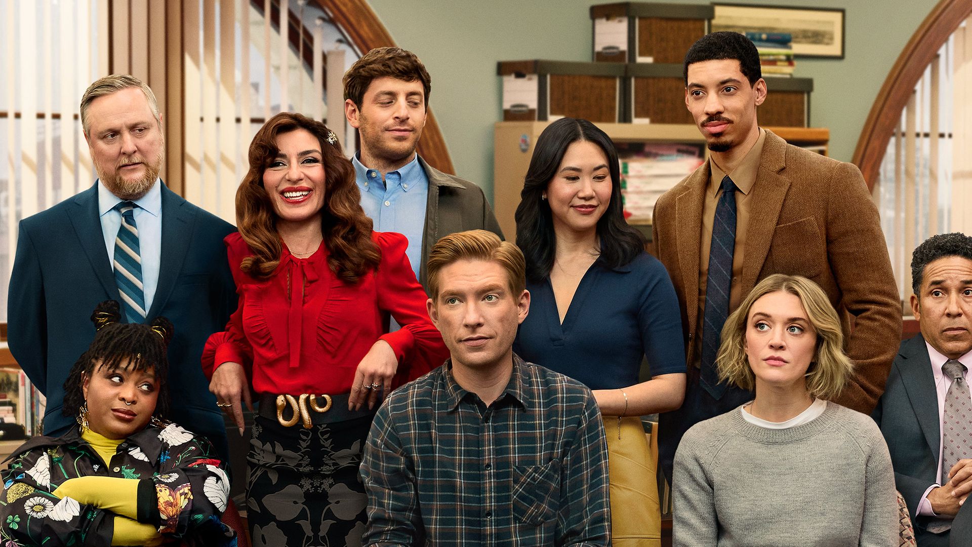 Nine people posing in an office with brown desks and shelves, some sitting on office chairs. Text reads "FROM THE CREW THAT BROUGHT YOU the office" and "the paper" in white.