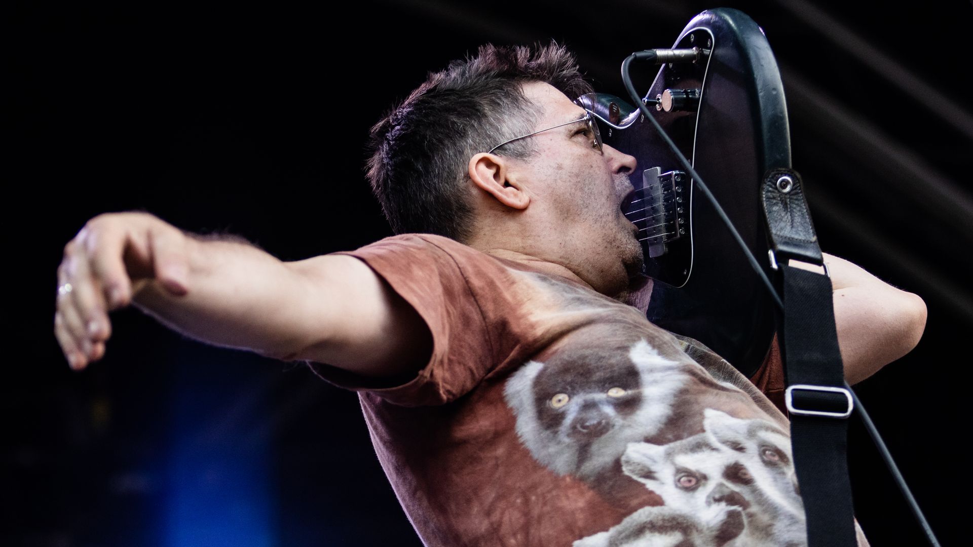 Photo of a ma on stage playing his guitar with his mouth 