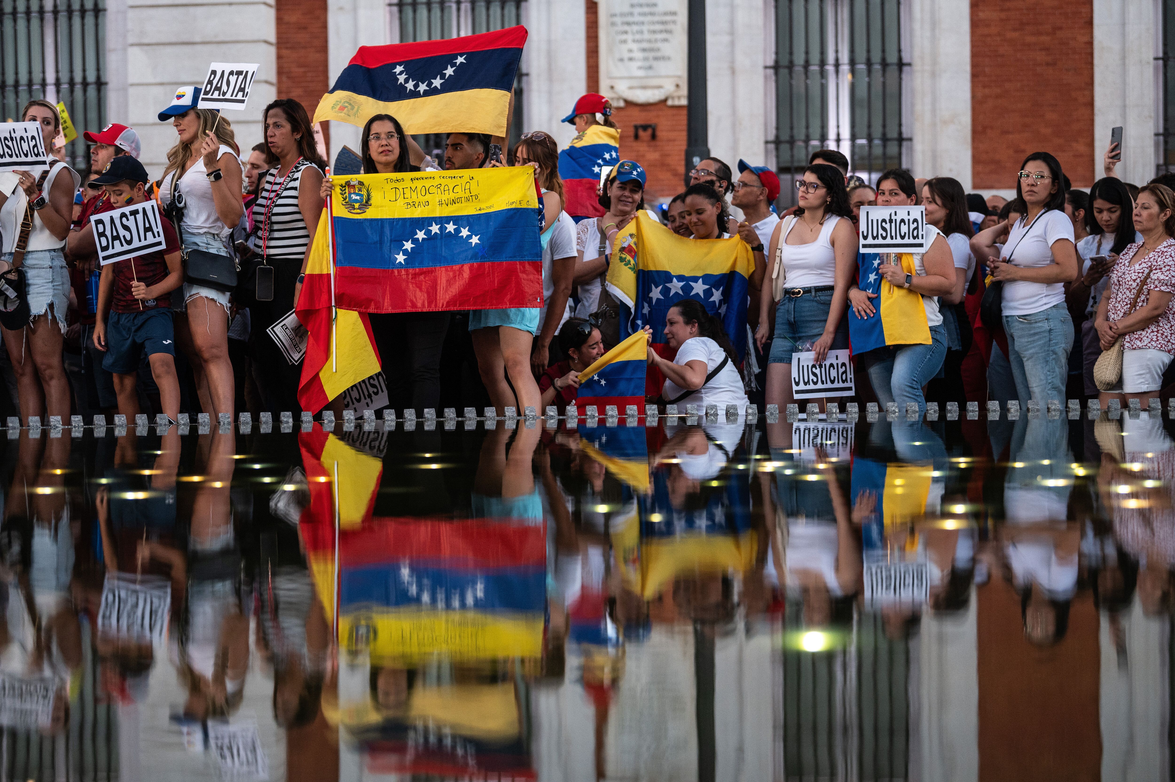 Protesters hold a Venezuelan flag near a body of water that shows their reflection. 