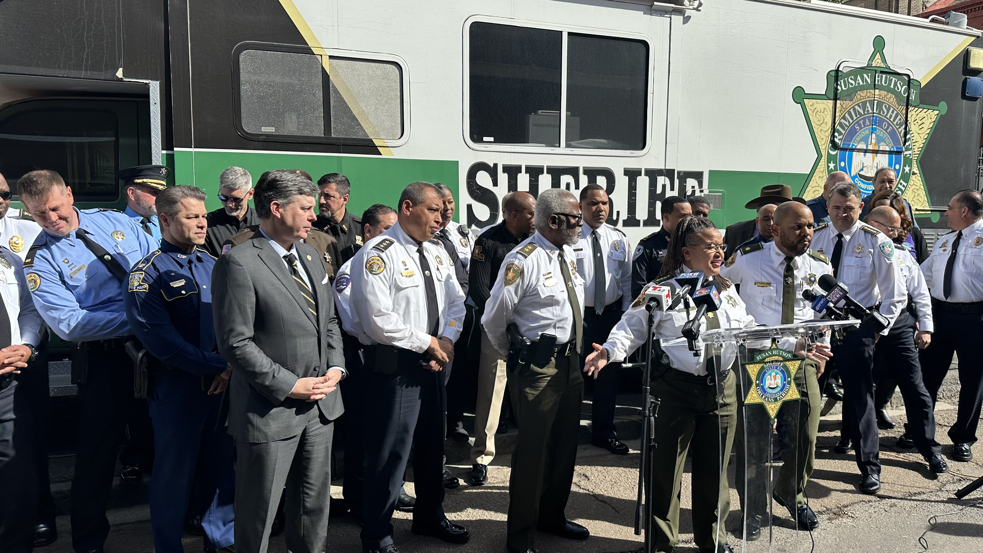 Orleans Parish Sheiff Susan Hutson speaks at a podium. She is flanked by over a dozen other regional law enforcement officers.