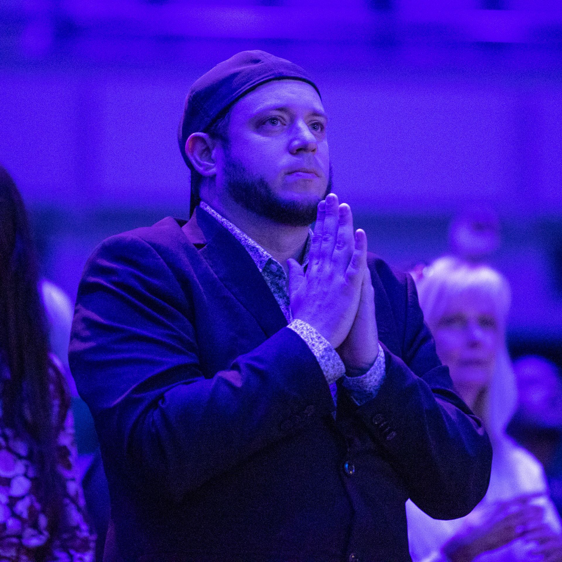 A bearded man in a backwards hat and suit, praying
