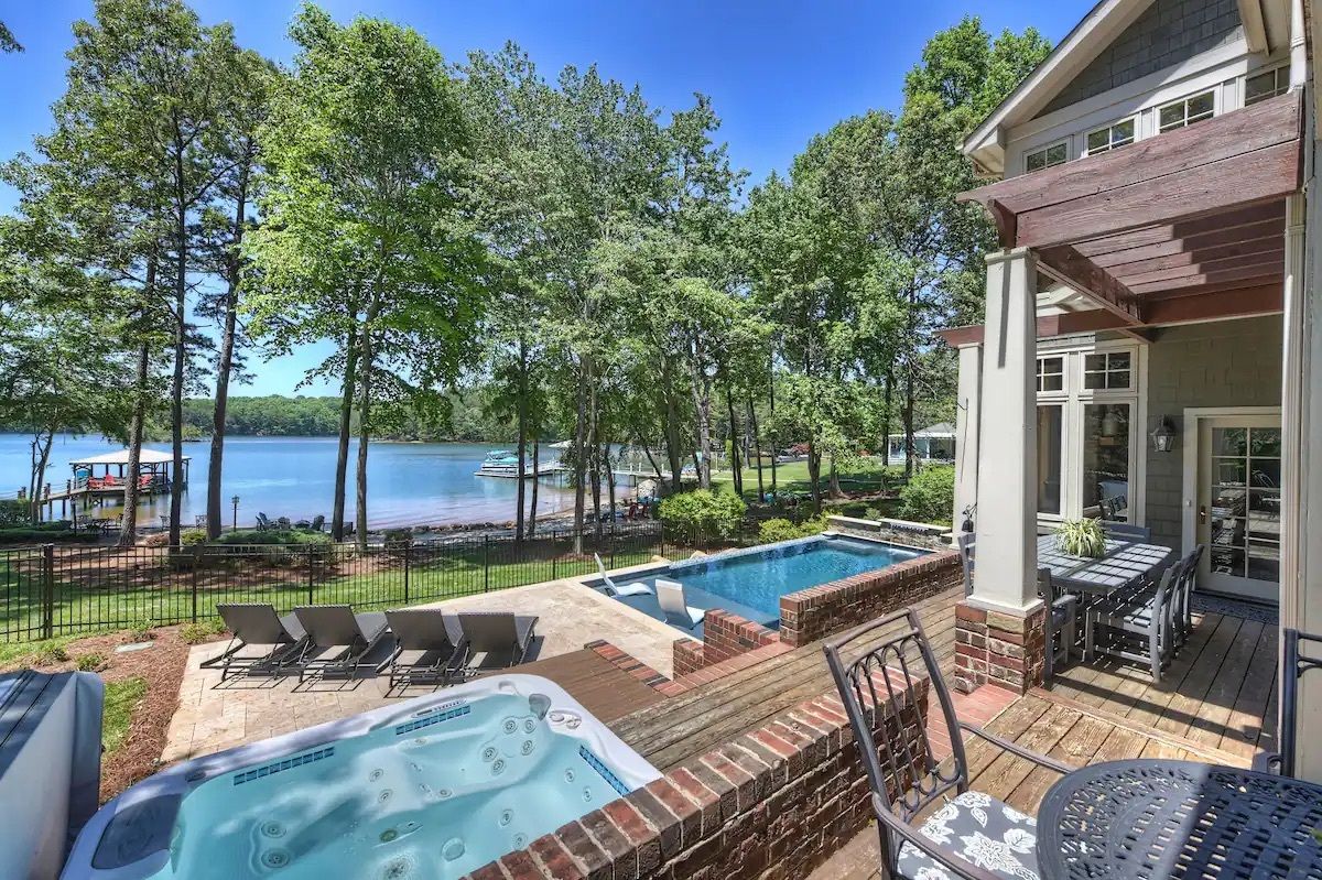 outside of mansion facing a lake wit a pool and hot tub