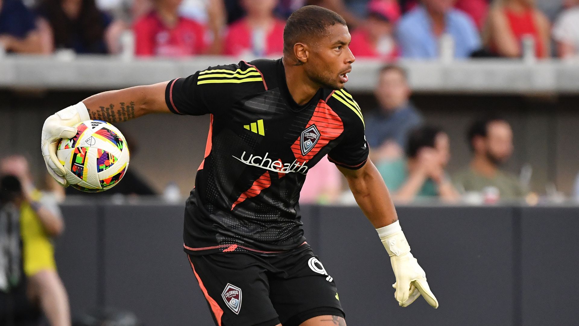 A man in a black jersey and white gloves prepares to throw a soccer ball. 