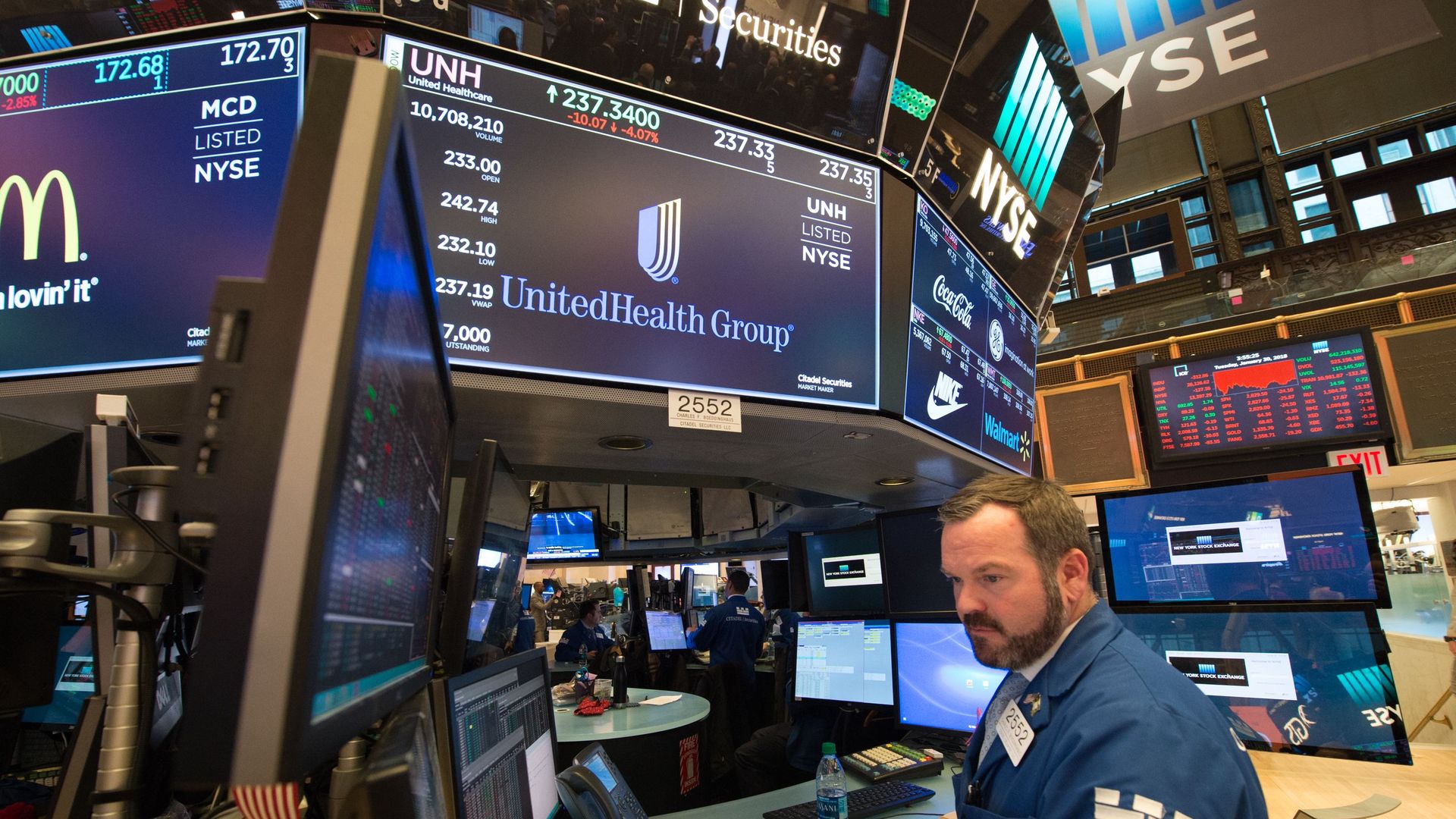 UnitedHealth Group's logo appears on a TV screen on a Wall Street trading floor with a broker standing underneath.