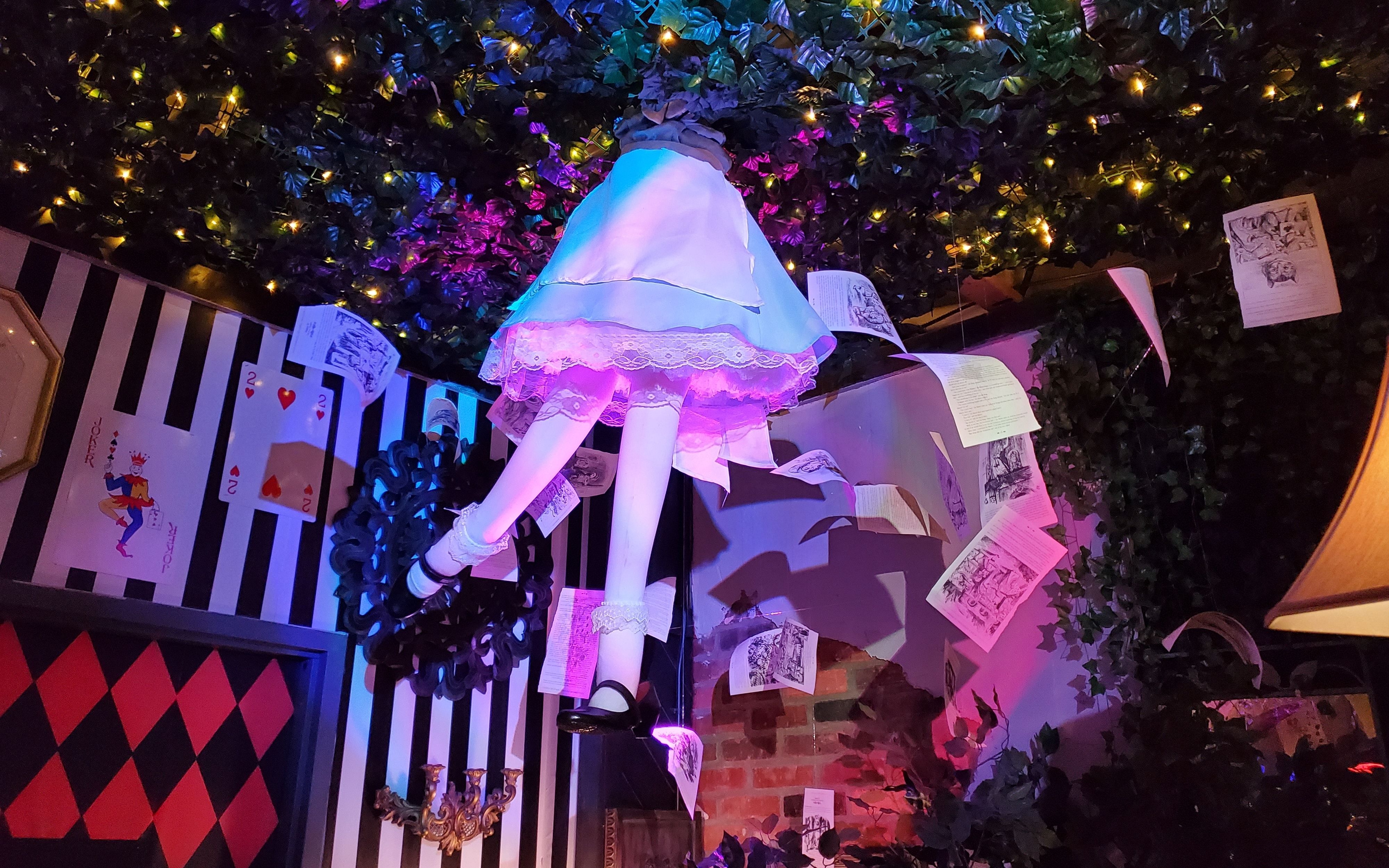 A mannequin of Alice in Wonderland's lower half and feet "falling" through a leaf-covered ceiling, surrounded by suspended book pages