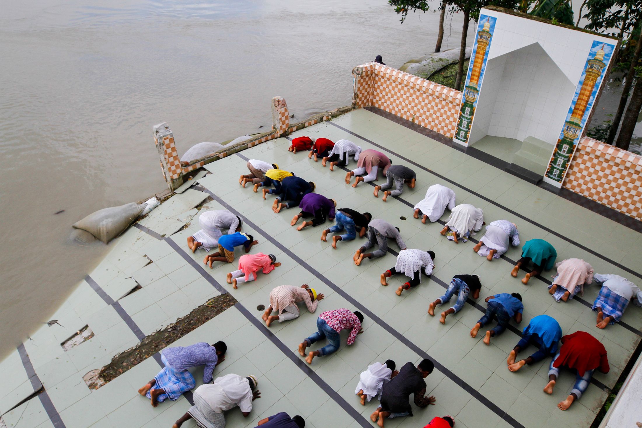 Rows of people kneel in prayer on a dock surrounded by water