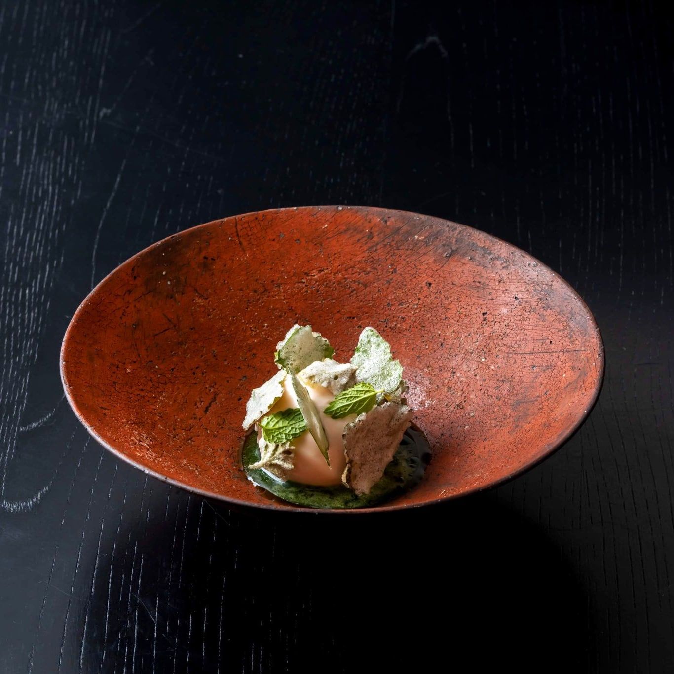A scoop of ice cream in a terra cotta bowl with herbs 
