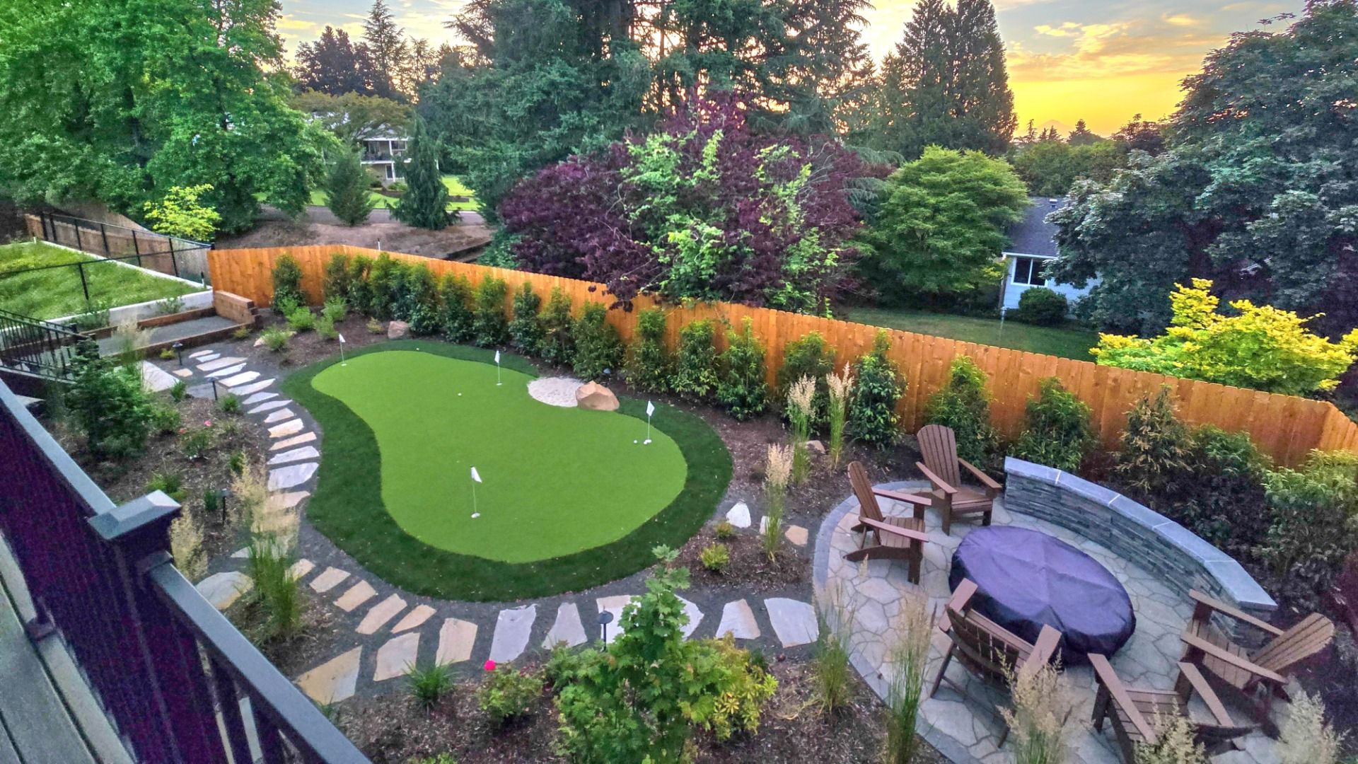 A backyard with a mini golf course, fire pit with wooden surrounding chairs, a stone walkway and bocce ball court.