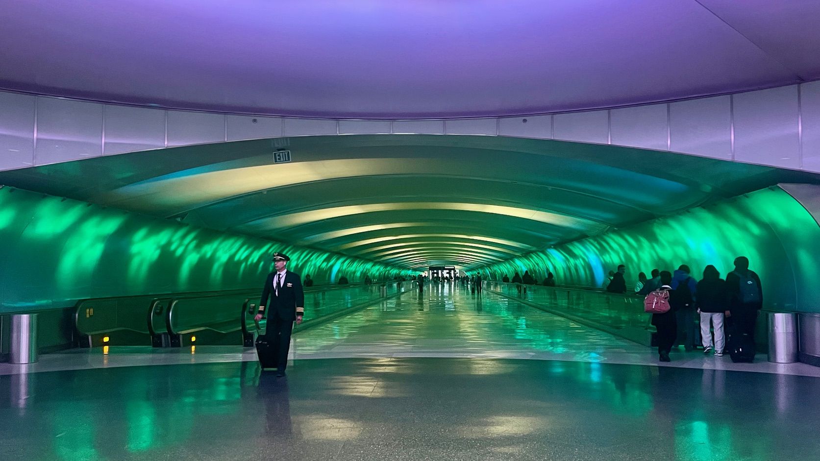 People walk through a tunnel with walkways on each side and green LED lights