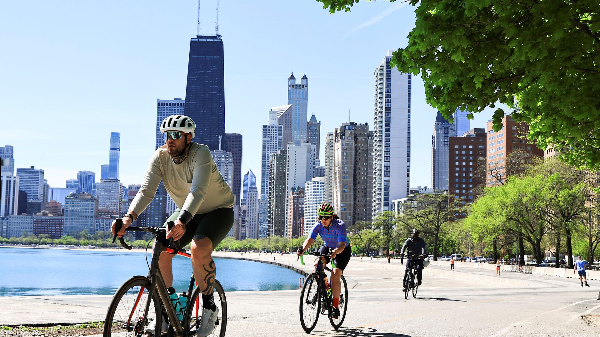 Photo: Bicyclists ride along a lake in front of buildings