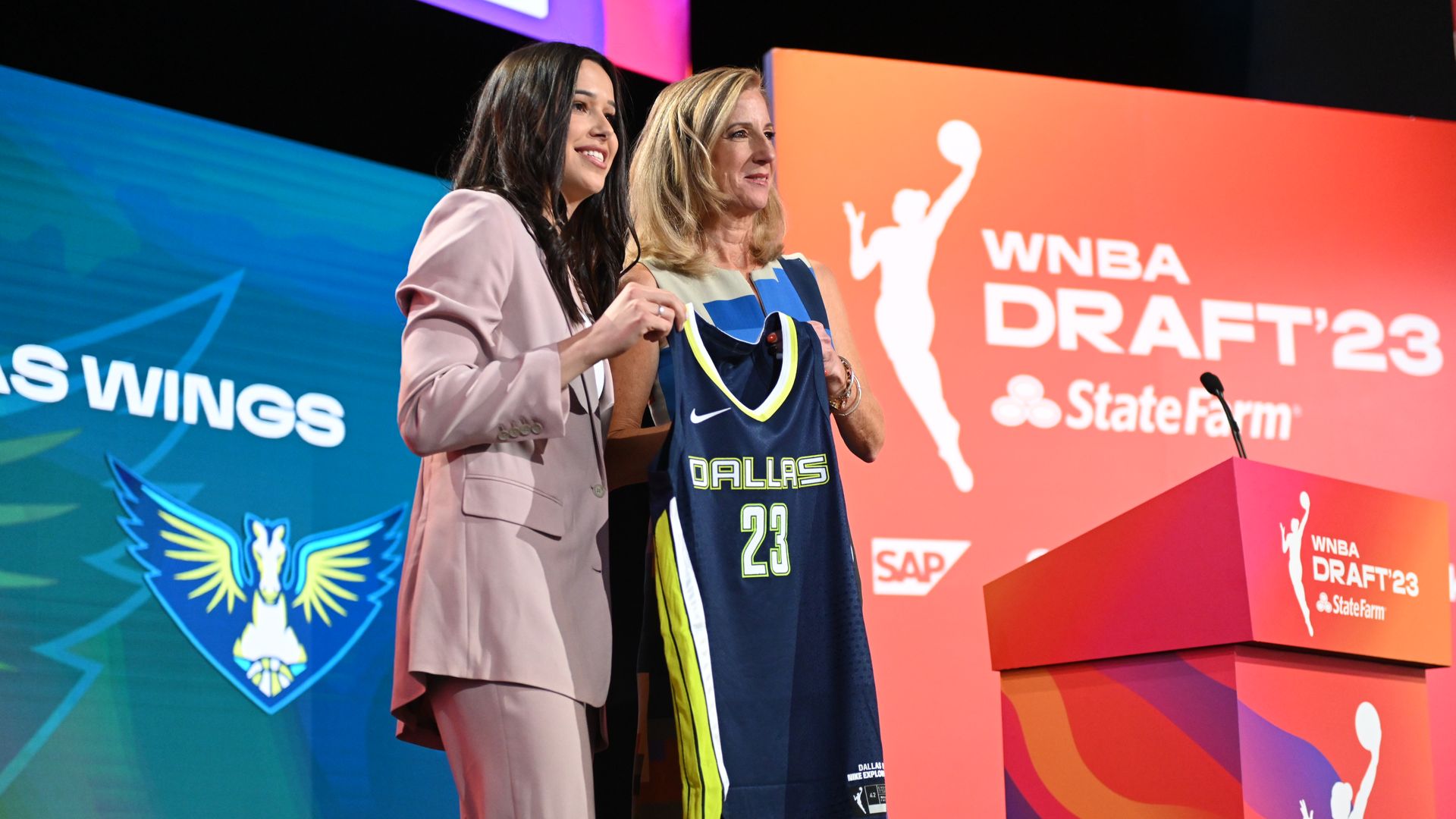 Two women hold up a blue jersey that says Dallas