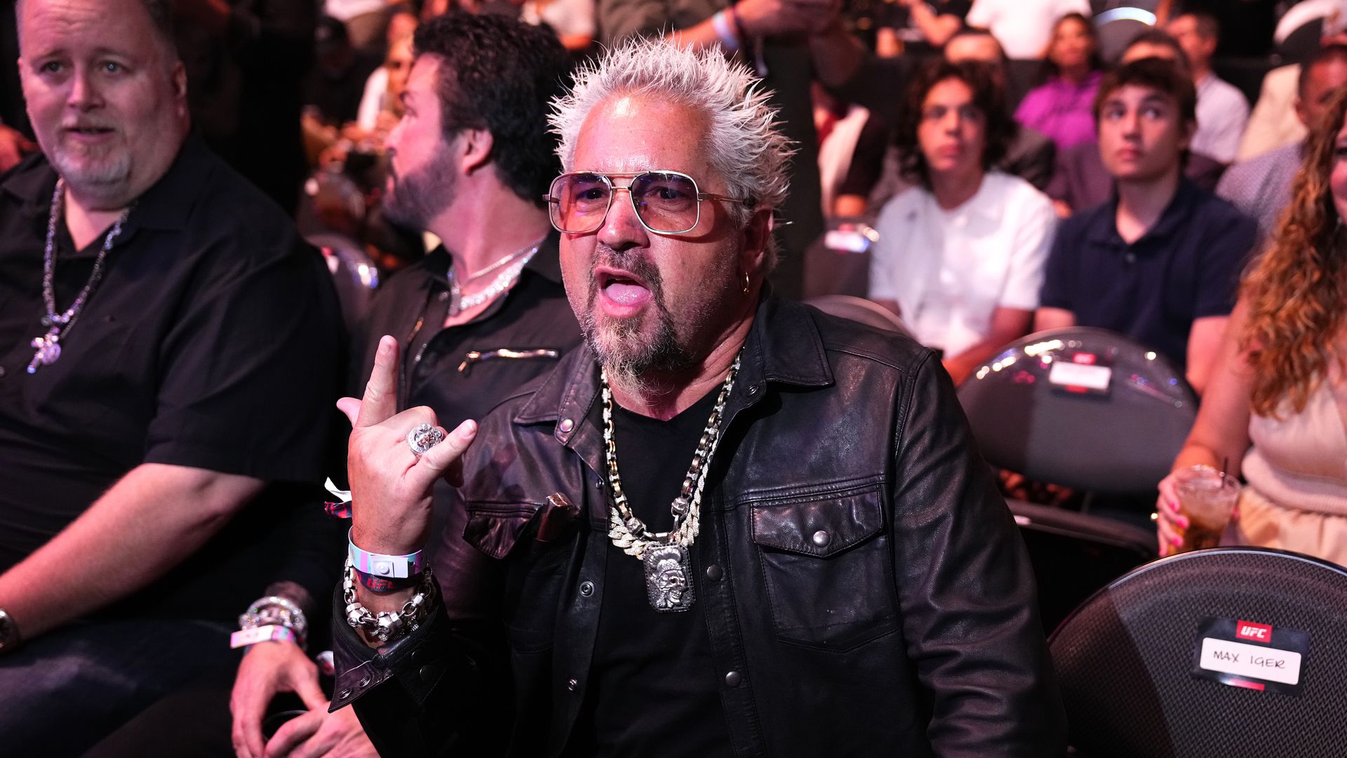 Guy Fieri making a "rock on" hand symbol in a stadium.