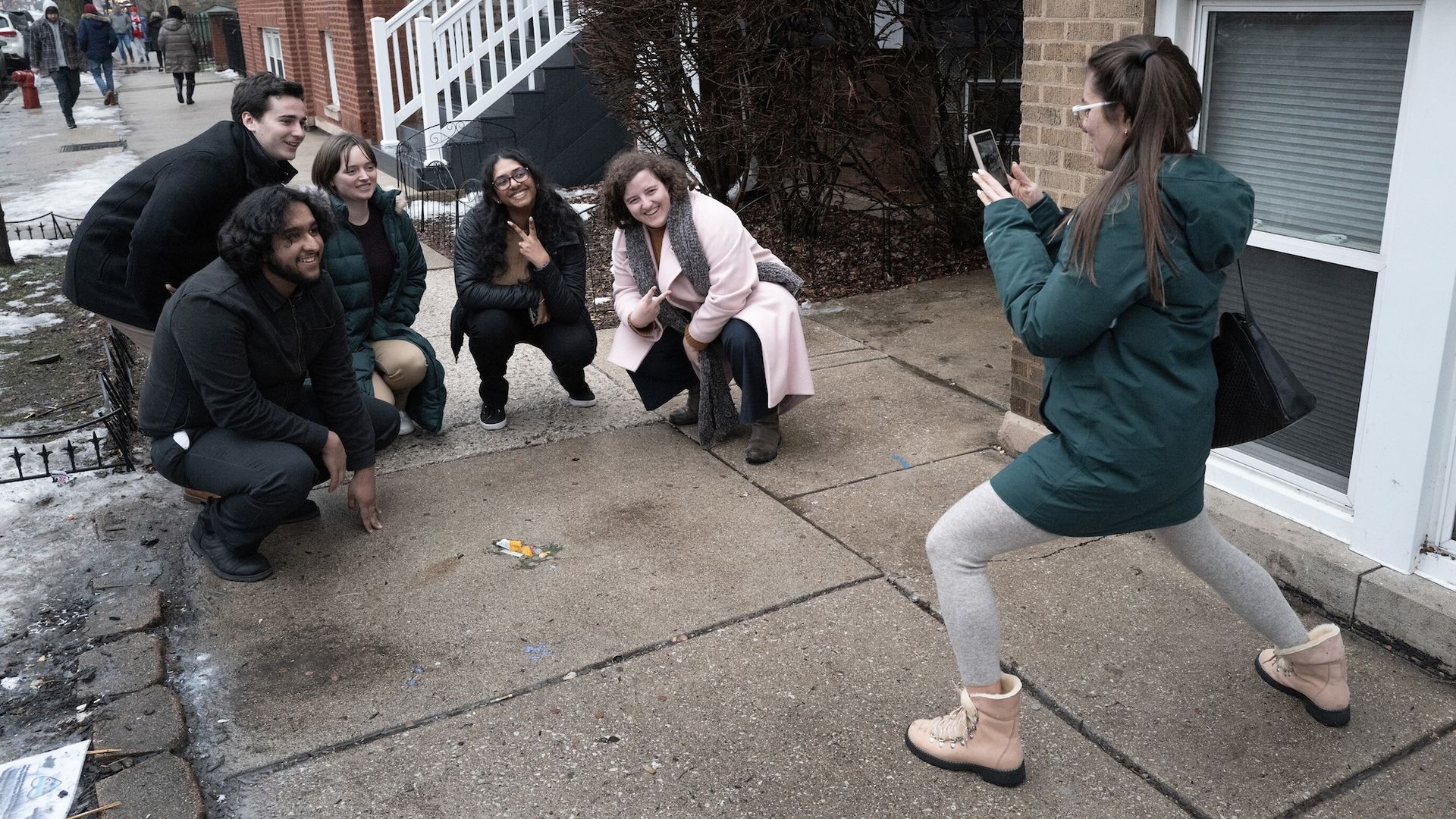 Five people crouch on sidewalk while another takes a photo.