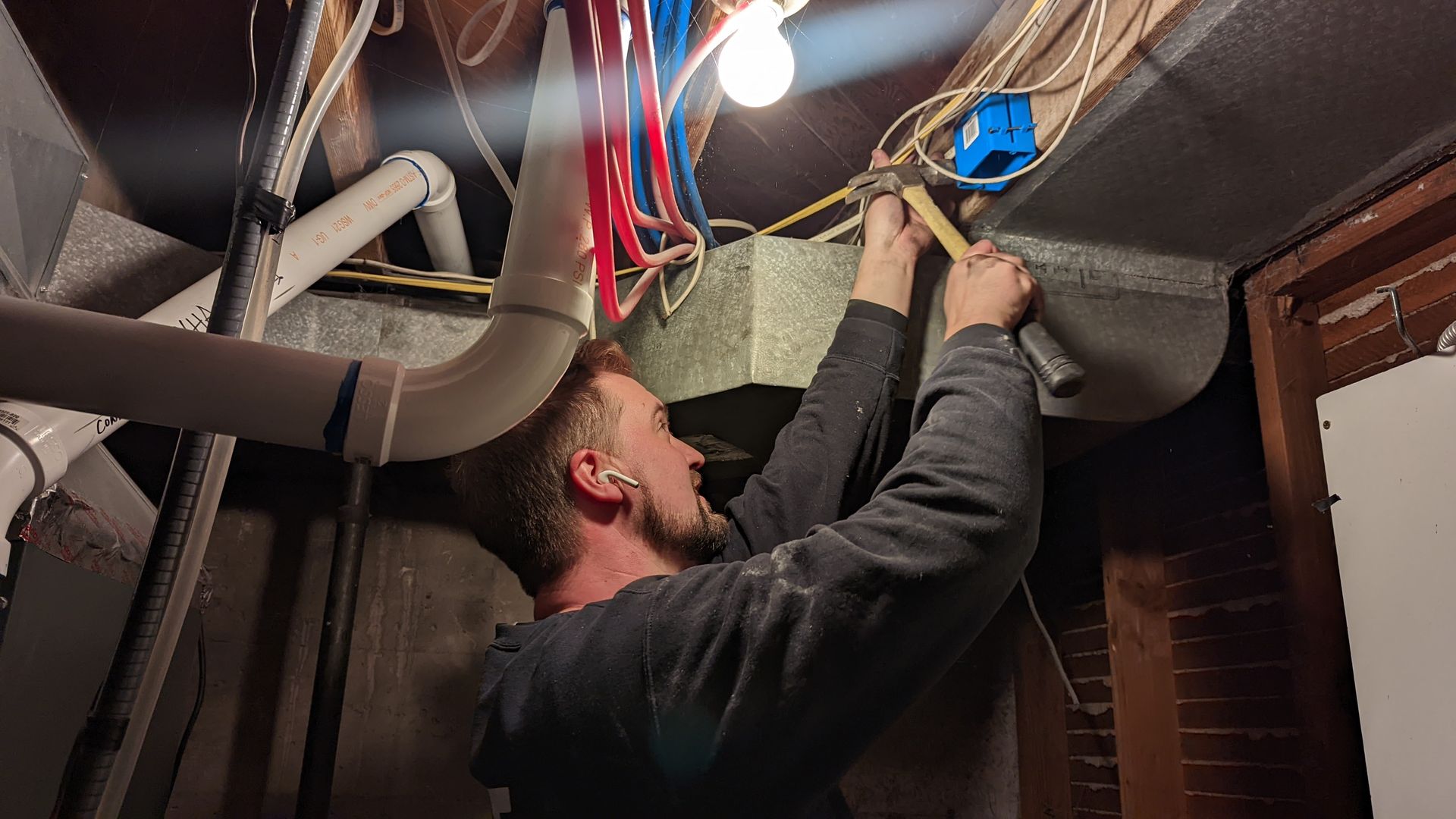 A man hammers a blue plastic square to a piece of wood in a basement.