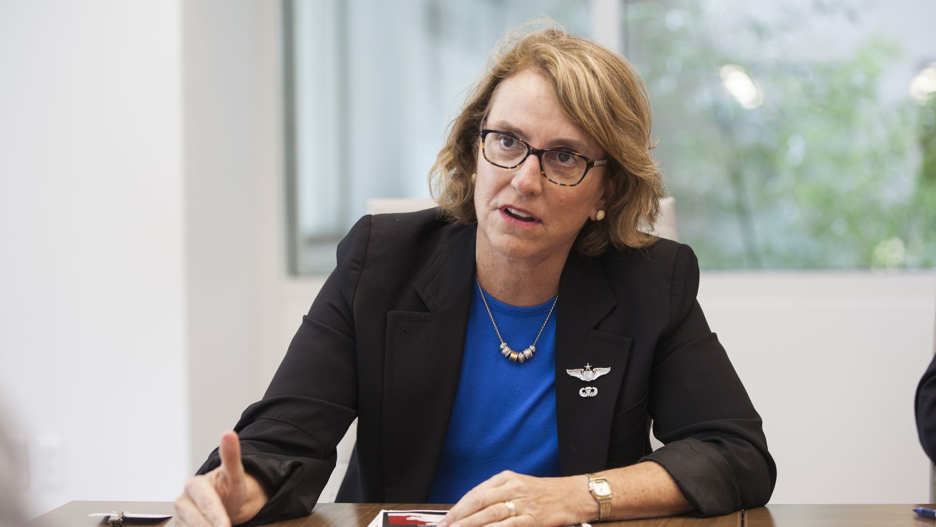A woman sits at a table and motions with her right hand while talking.