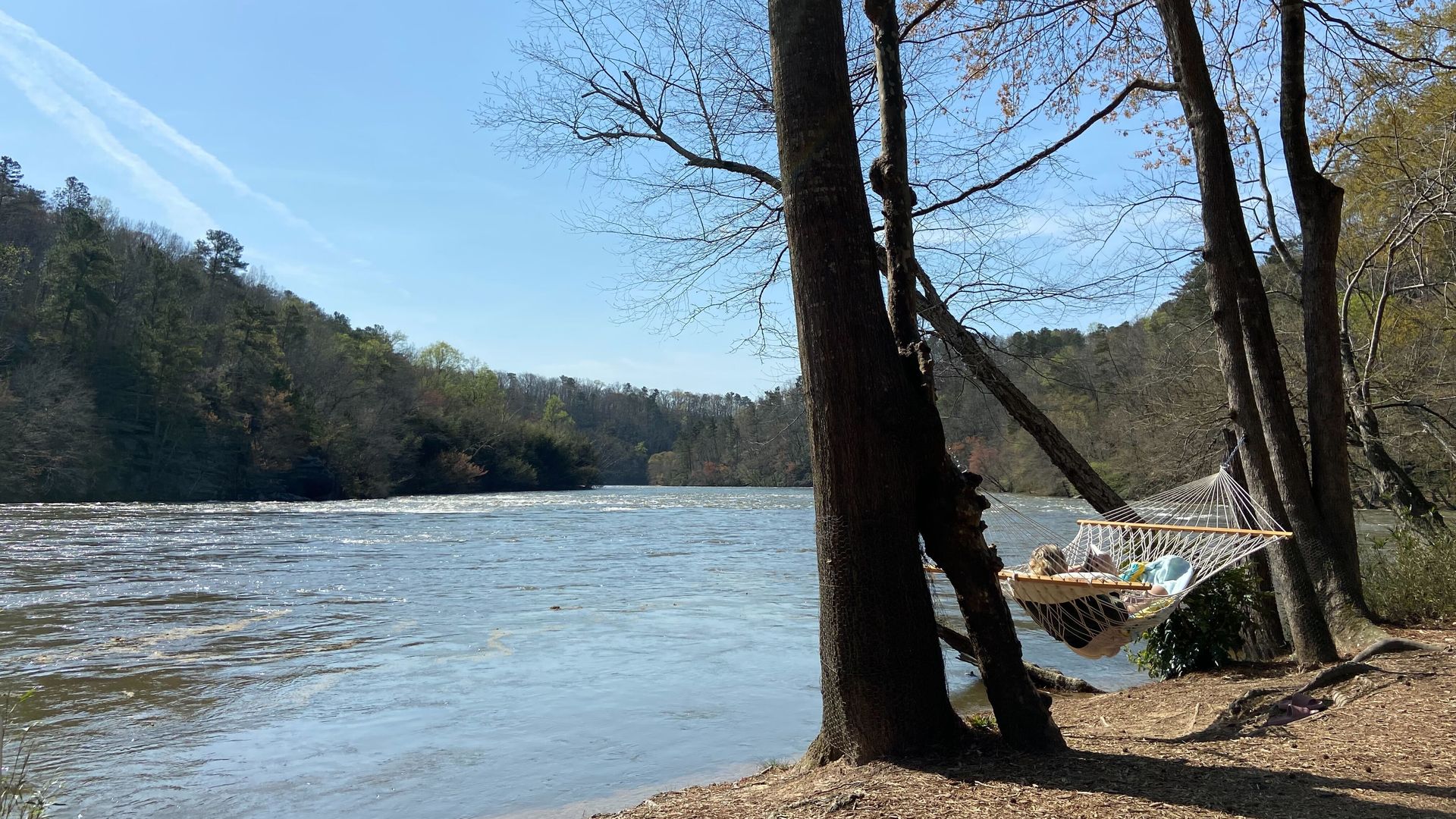 A person sits in a hammock on a sunny day alongside the Chattahoochee River