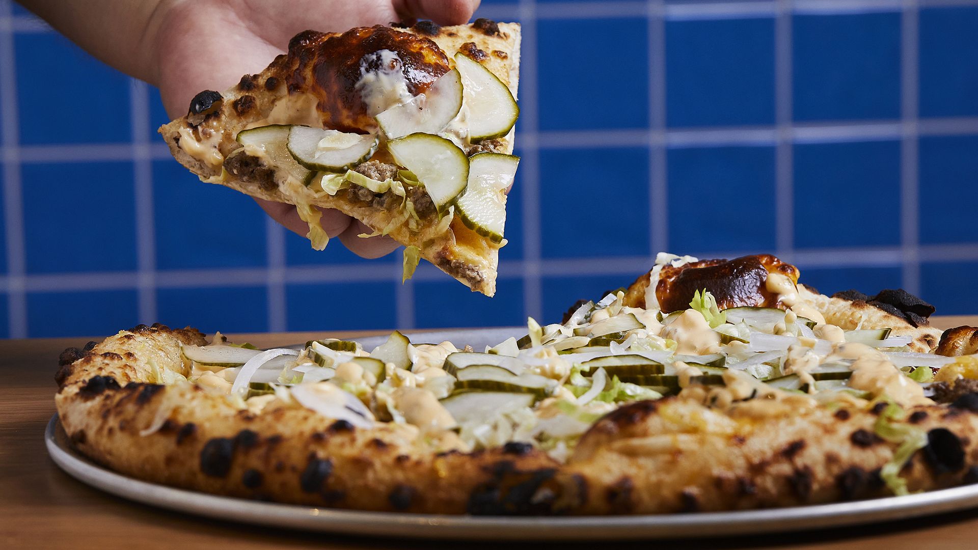 A hand picks up a slice of the Harambe Loved Big Macs pizza at Boogy & Peel photographed in Washington, DC on July 29, 2022. (Photo by Deb Lindsey for The Washington Post via Getty Images).