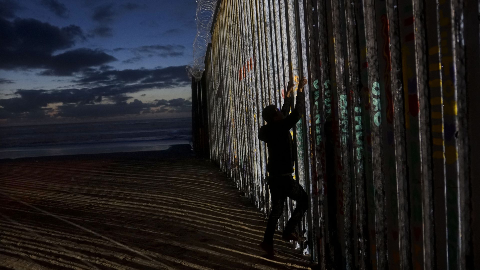 Man climbs border wall in Tijuana.