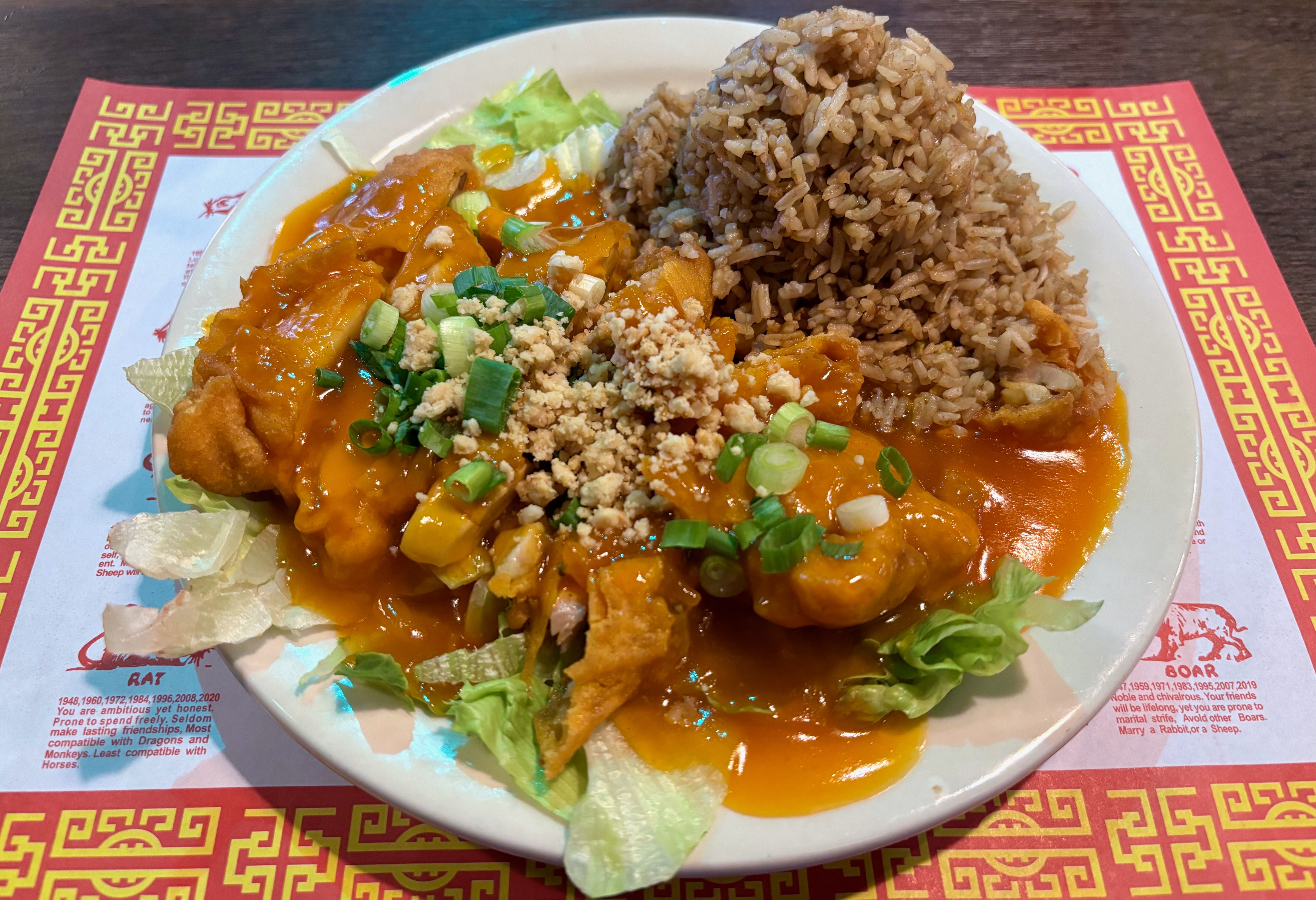 A plate of Wor Sue Gai, a boneless chicken topped with orange gravy, scallions and crushed nuts, with a side of fried rice