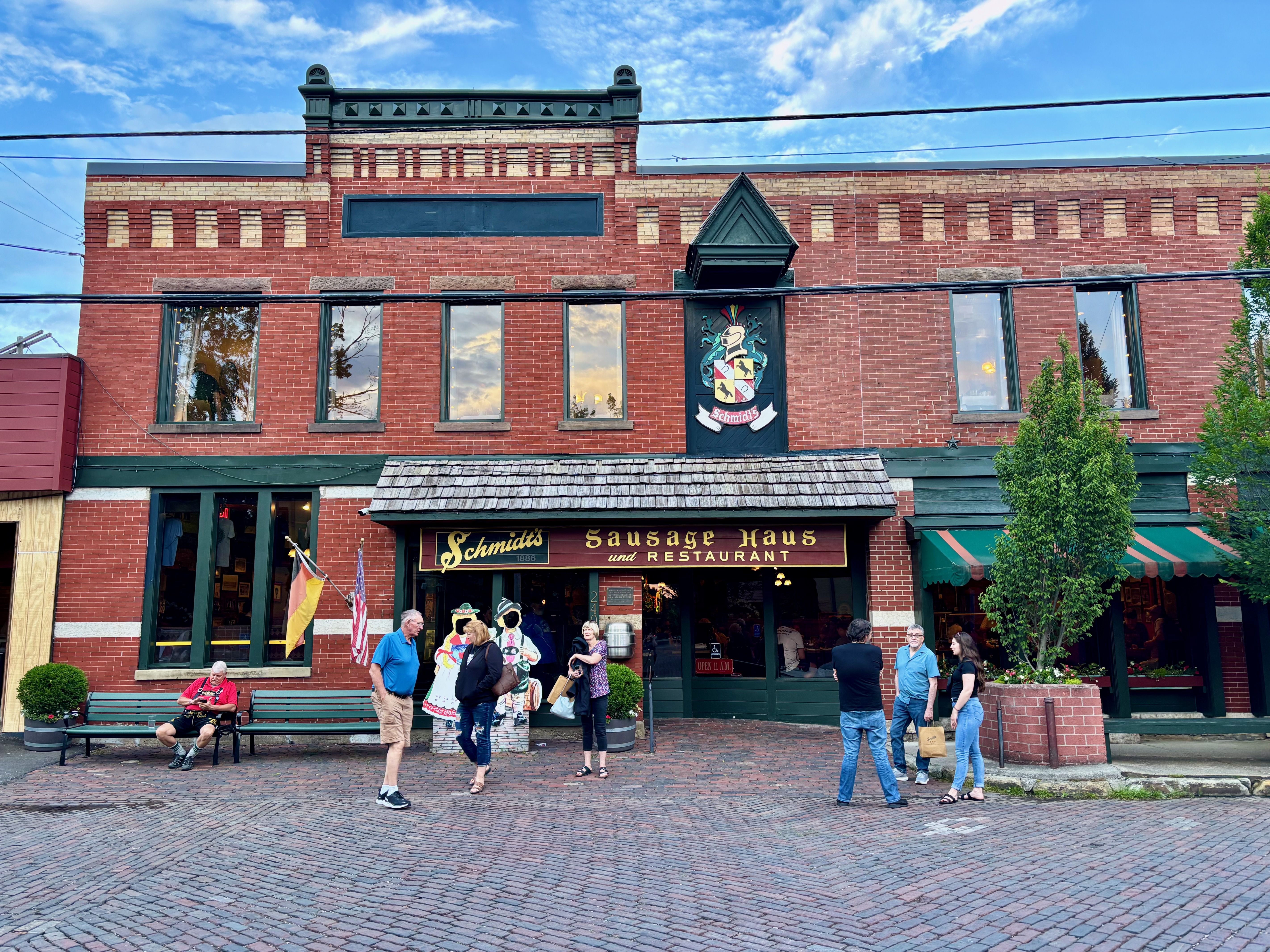 The brick exterior of Schmidt's Sausage Haus, with several people waiting outside for tables on a brick-lined street