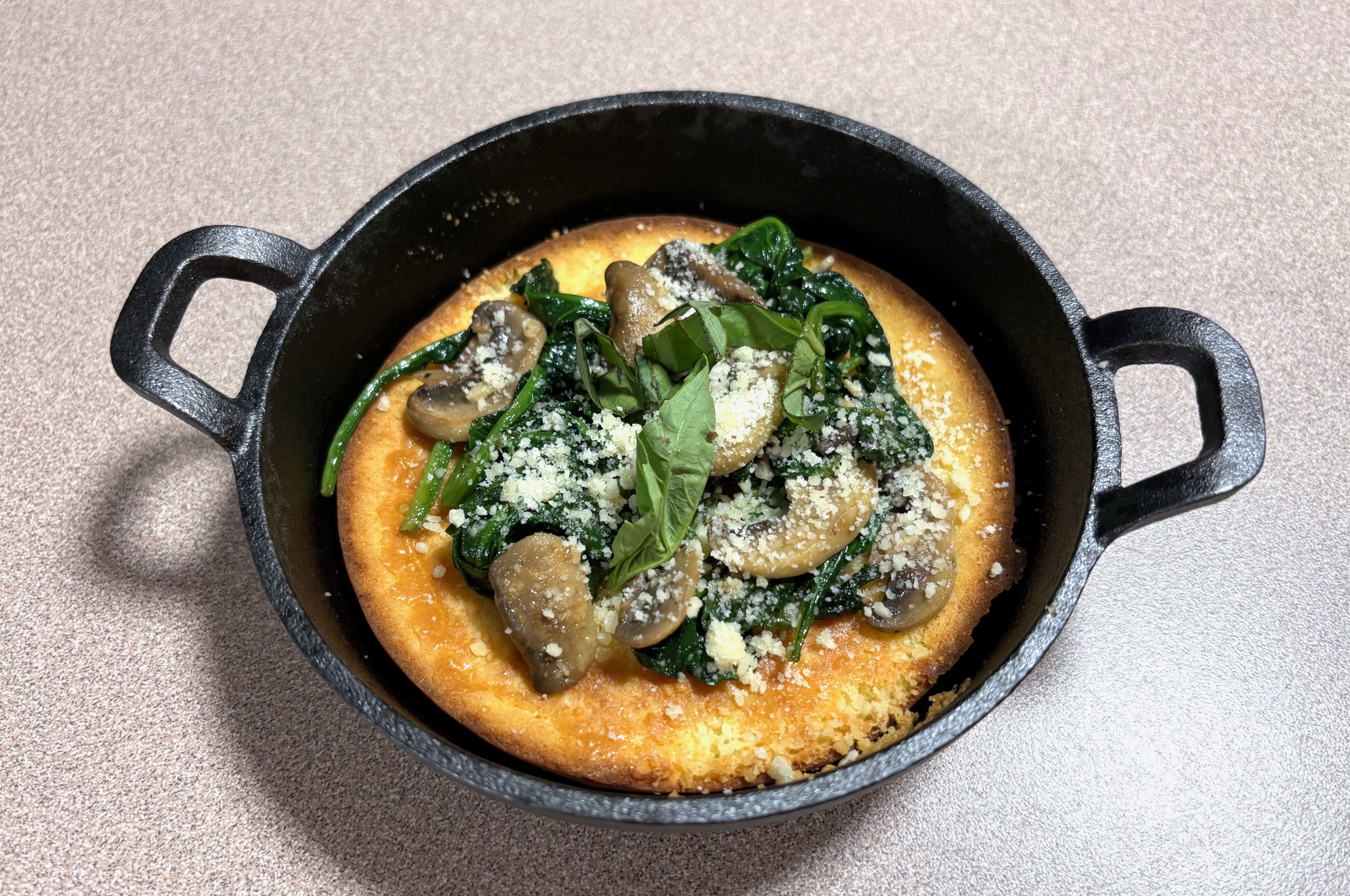 A dutch baby in a mini cast-iron skillet, topped with mushrooms, parmesan cheese, spinach and basil