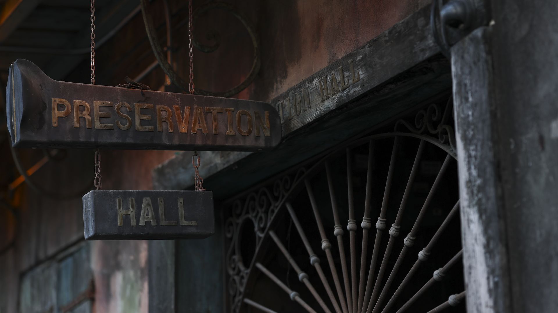 A photo of the exterior of Preservation Hall. A sign saying the venue's name on two aged plaques hangs from a chain outside the gate.