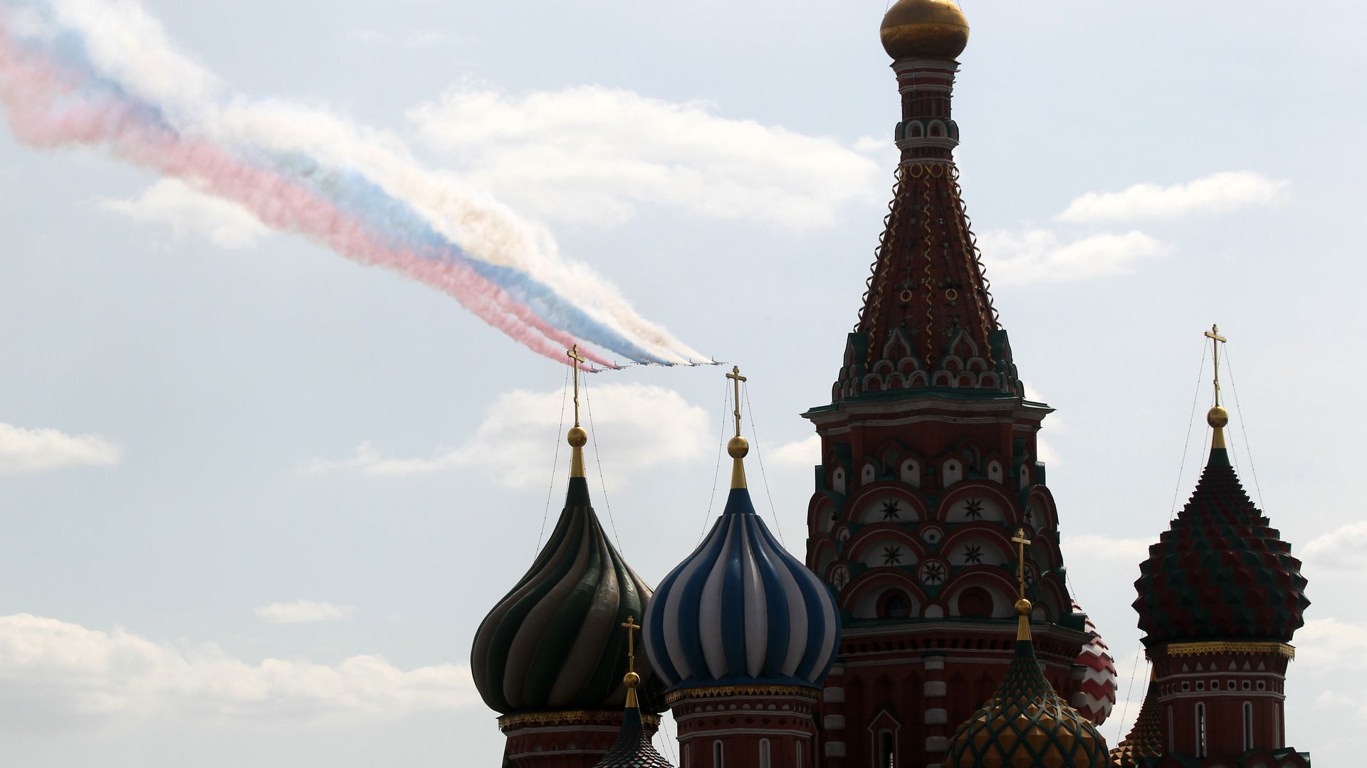 Photo of fighter jets demonstrating the colors of the Russian flag as they fly over buildings