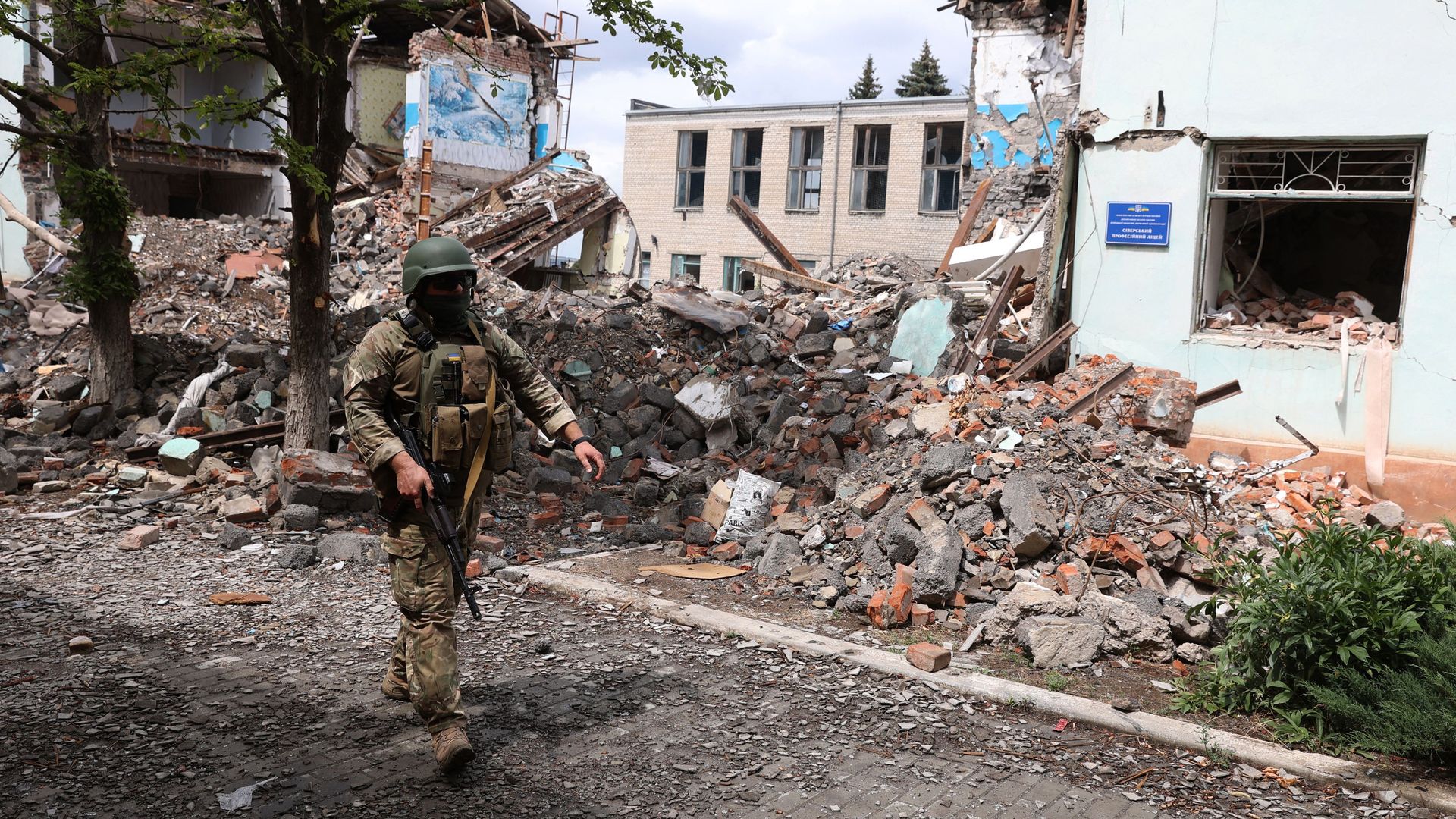 A Ukrainian serviceman passes by destroyed buildings
