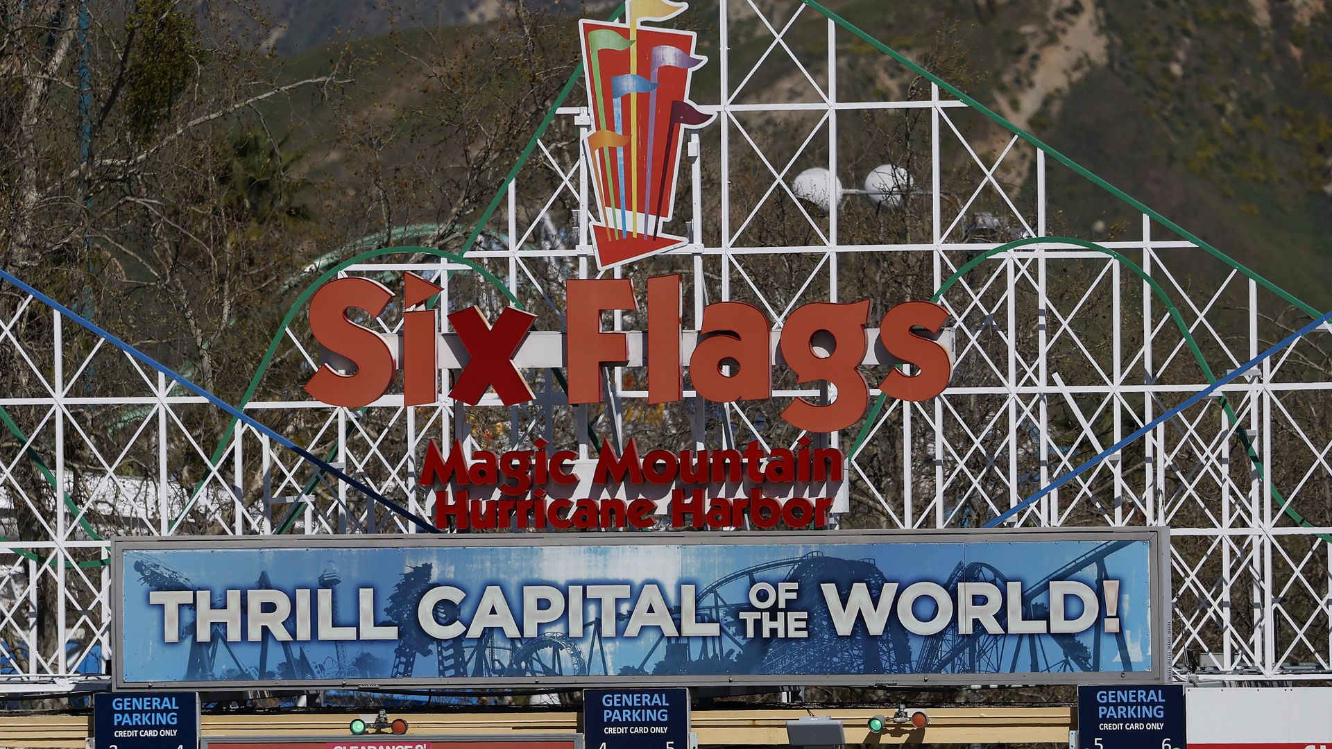 The entrance to Six Flags Magic Mountain Hurricane Harbor with the full park name in a big sign, and another reading "Thrill Capital of the World!," with roller coaster designs in the background. 