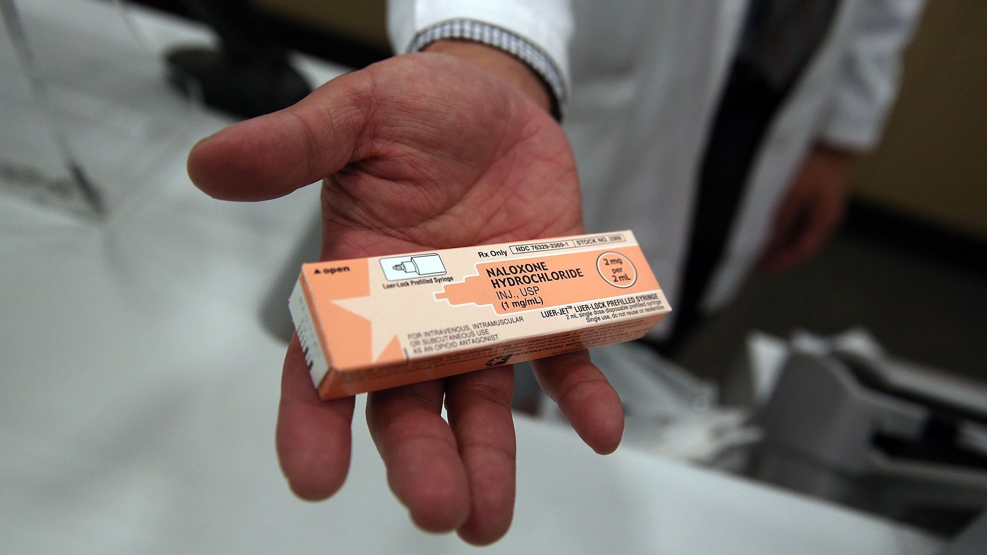 In this image, a doctor holds an orange prescription box of Oxycontin pills up to the camera. 