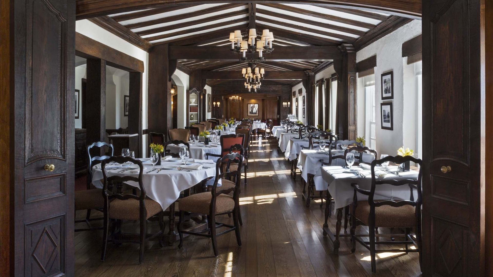 A long wooden hallway with dining room tables. 