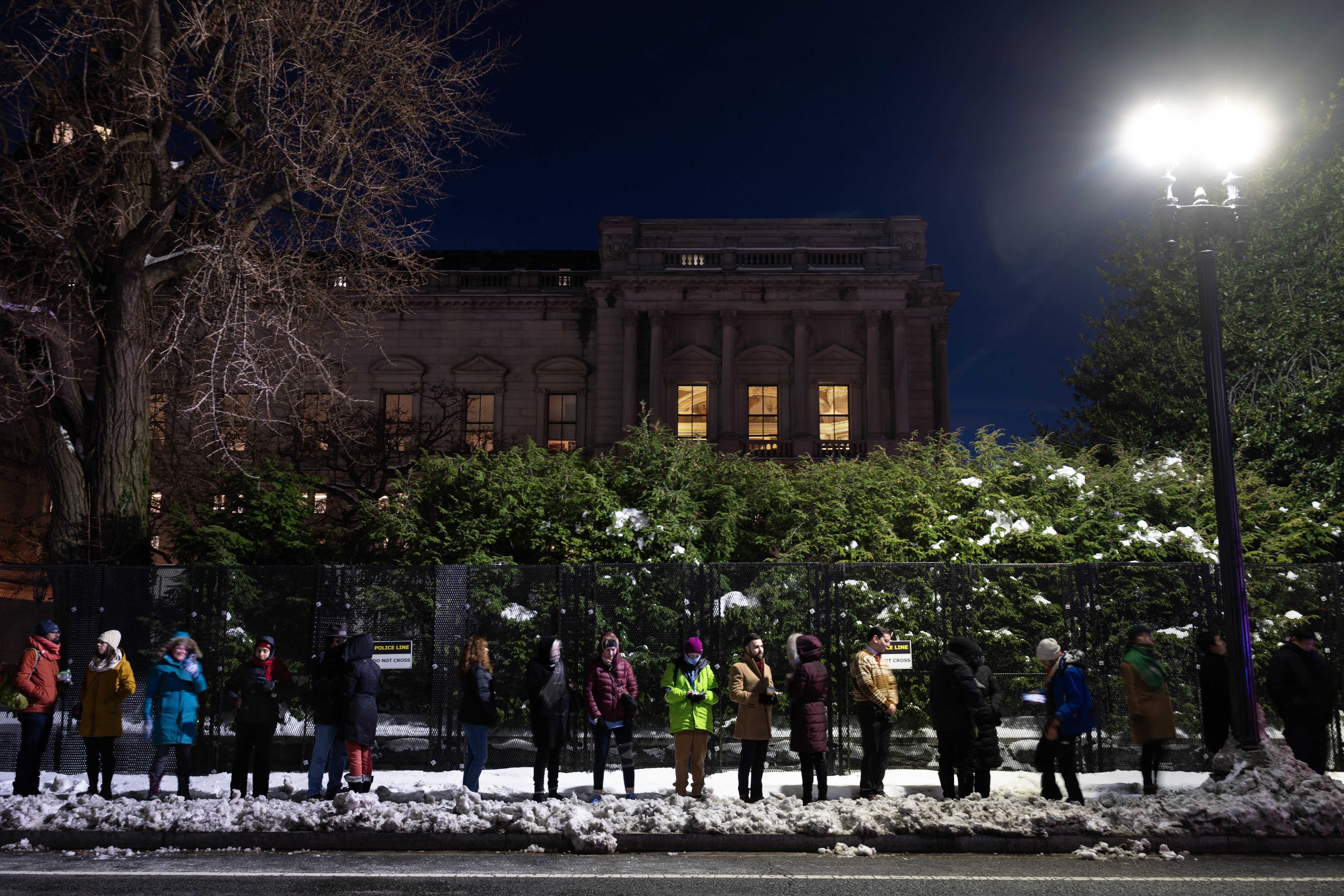 A photo shows a line of people waiting outside on the street at night in Washington, D.C.