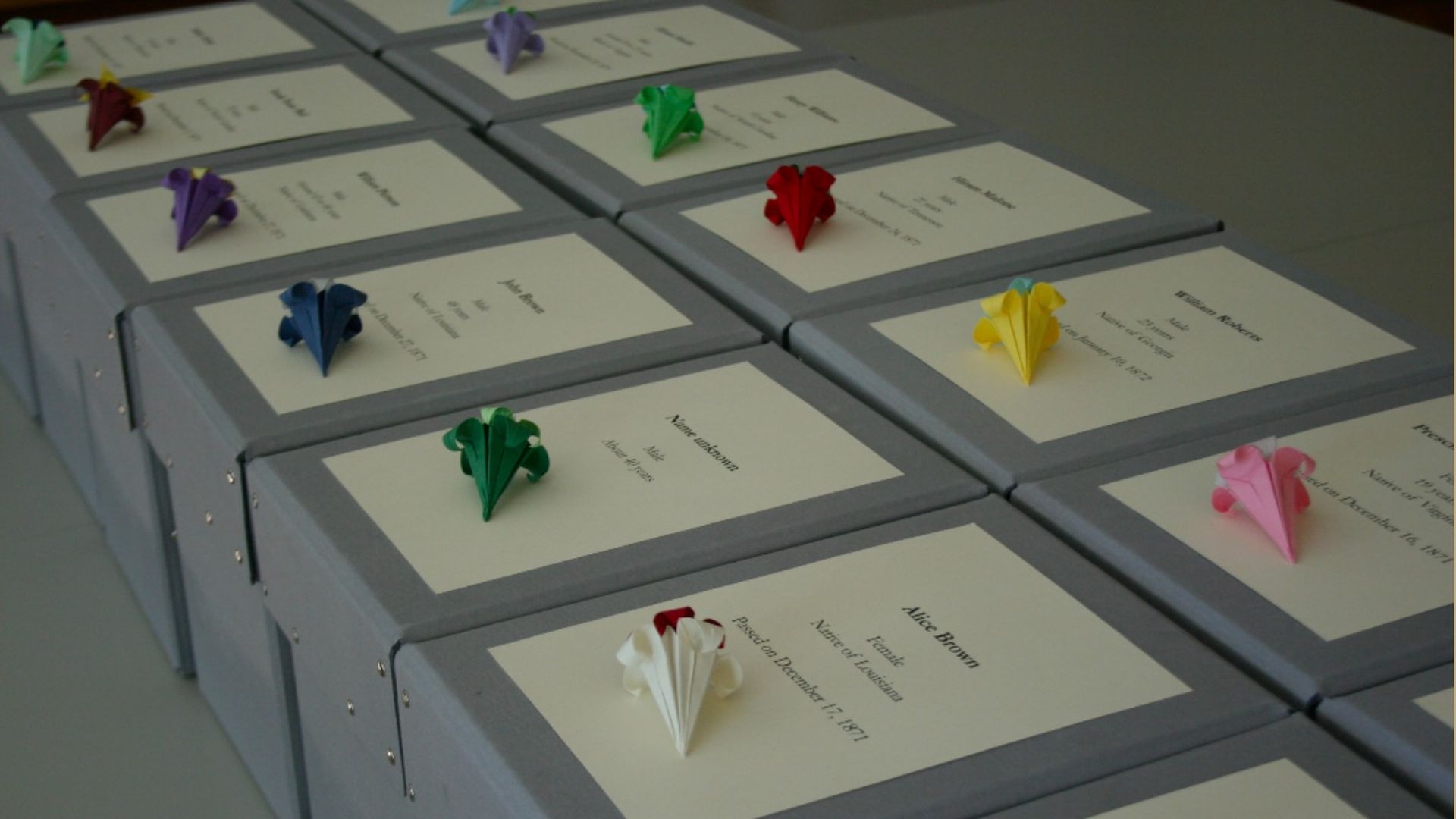Gray boxes are stacked next to each other with paper flowers and names labeled on top.