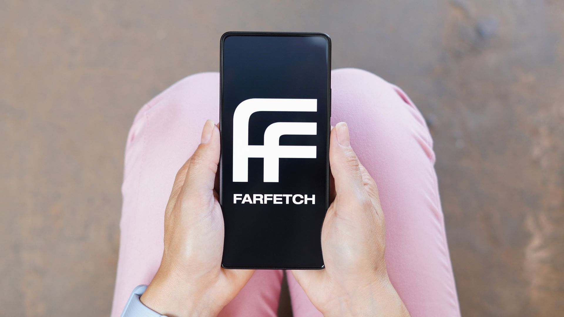A photo of someone holding a phone displaying the FarFetch logo