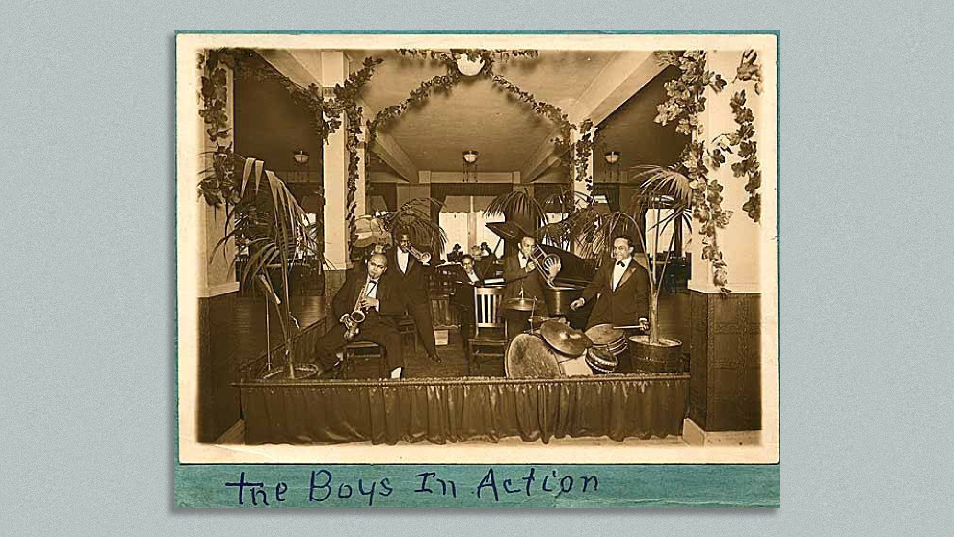 An old photo of a jazz band, in black and white, with "the boys in action" written below the photo. Mounted on a gray background.