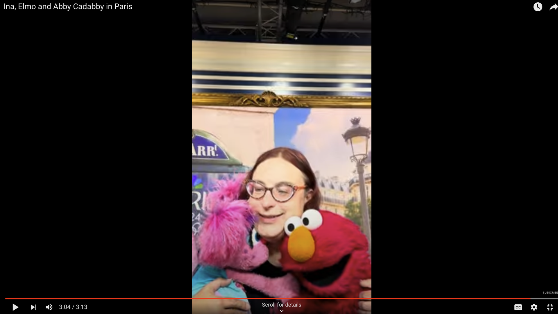 A photo showing a screenshot of a YouTube video that appears to be shot on a phone. In the image, you see Axios reporter Ina Fried hugging Abby Cadabby on the left and Elmo on the right.
