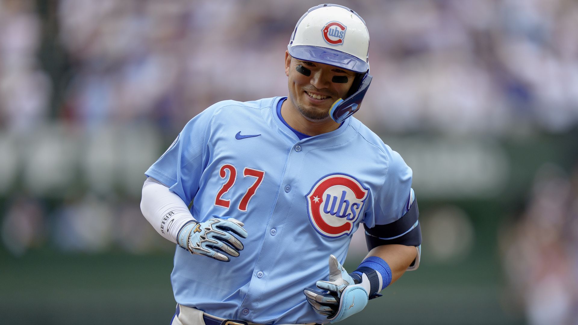 Photo of a baseball player in uniform trotting around the basepaths in a stadium. 