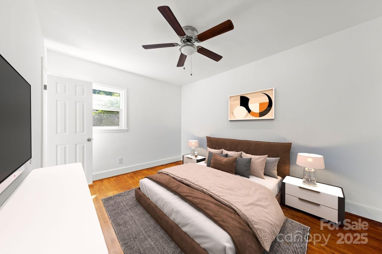 Modern bedroom with white walls, wooden floor, ceiling fan, brown and beige bedding, two white nightstands with lamps, abstract wall art, and a large TV on opposite wall.