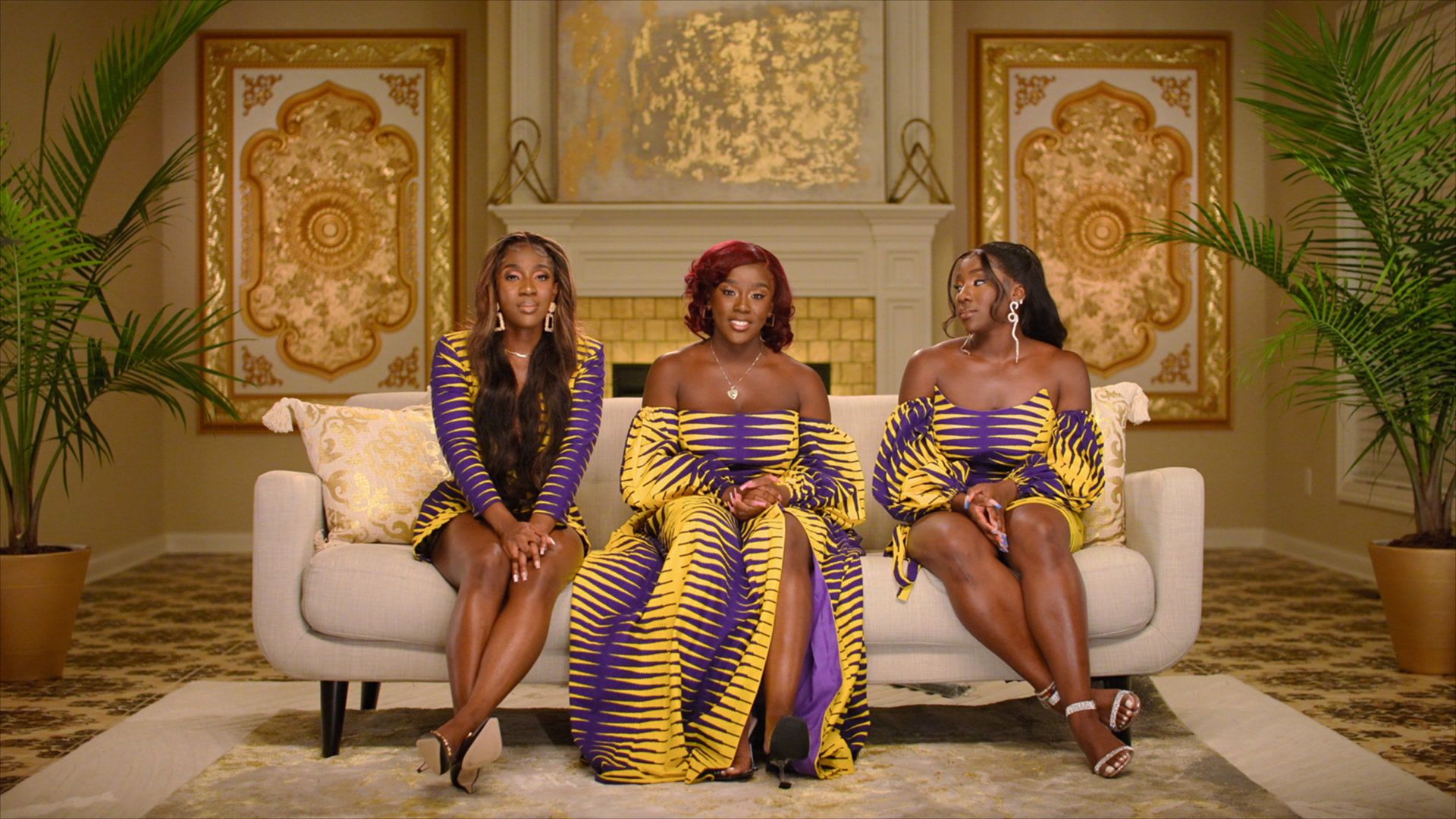 Three Agyekum sisters sit on a couch in an opulent room. 
