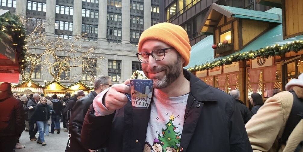 Photo of a man drinking from a cup outside in a plaza 