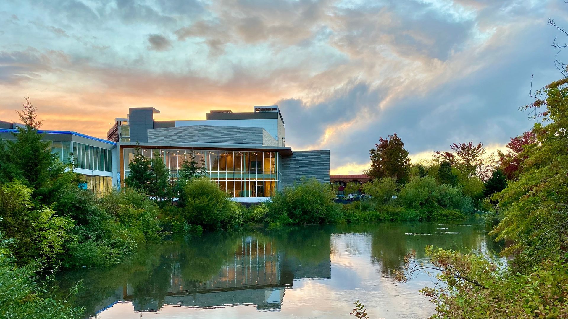 Concrete and glass performance center next to a creek under a sunset