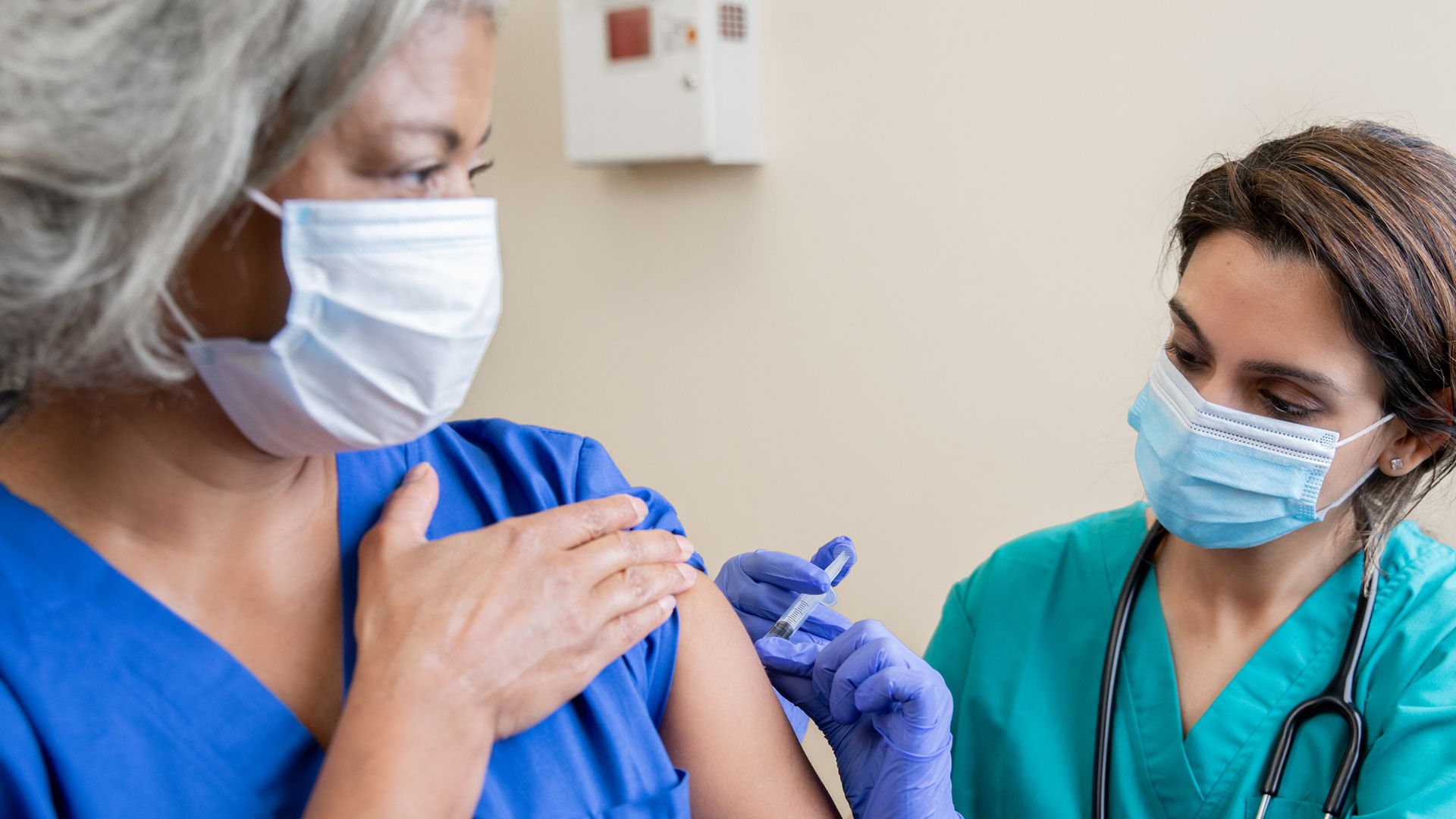female healthcare worker administers COVID-10 vaccination into left arm of an older female recipient