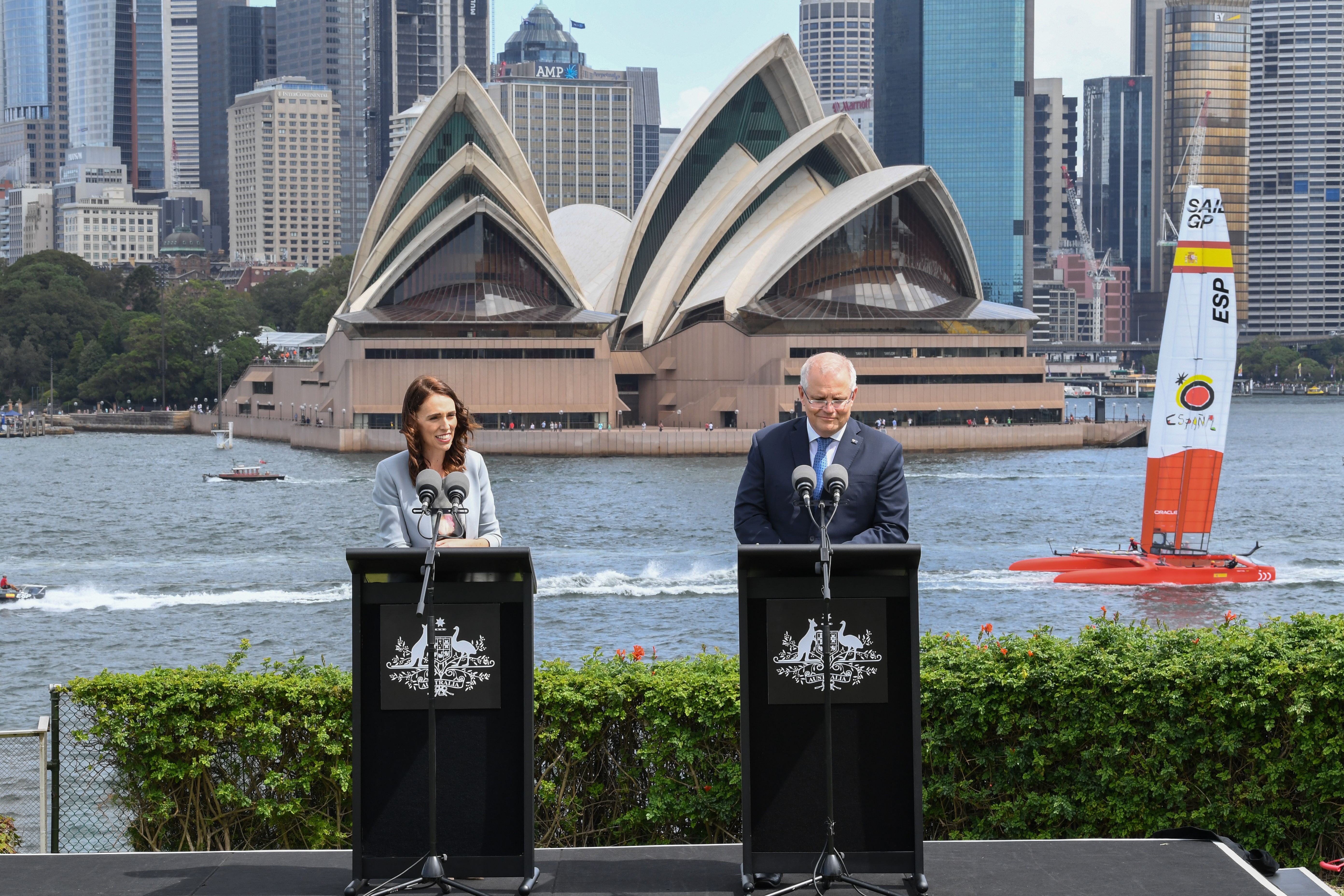 The prime ministers of New Zealand and Australia at podiums with the Sydney Opera House in the background.