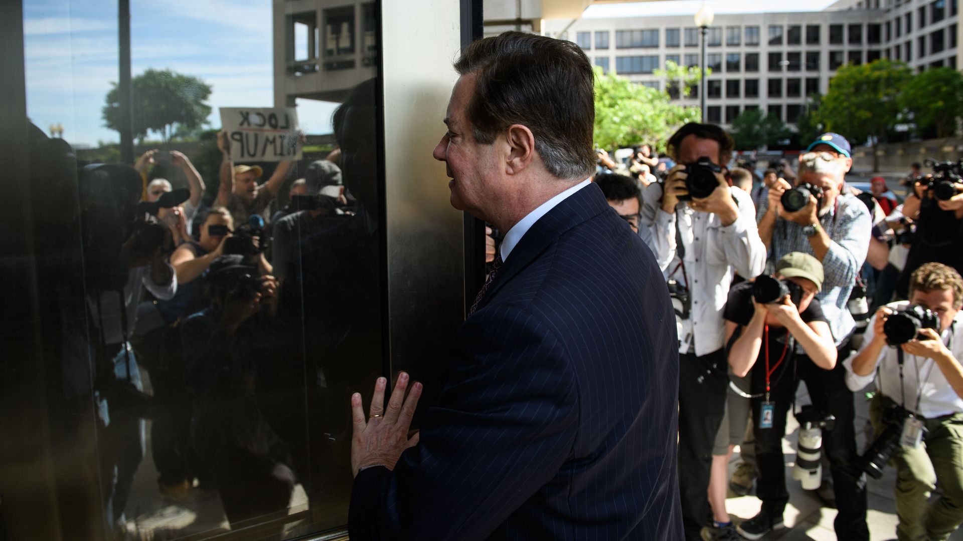 Paul Manafort pushes on a reflecting door while photographers take photos of him.