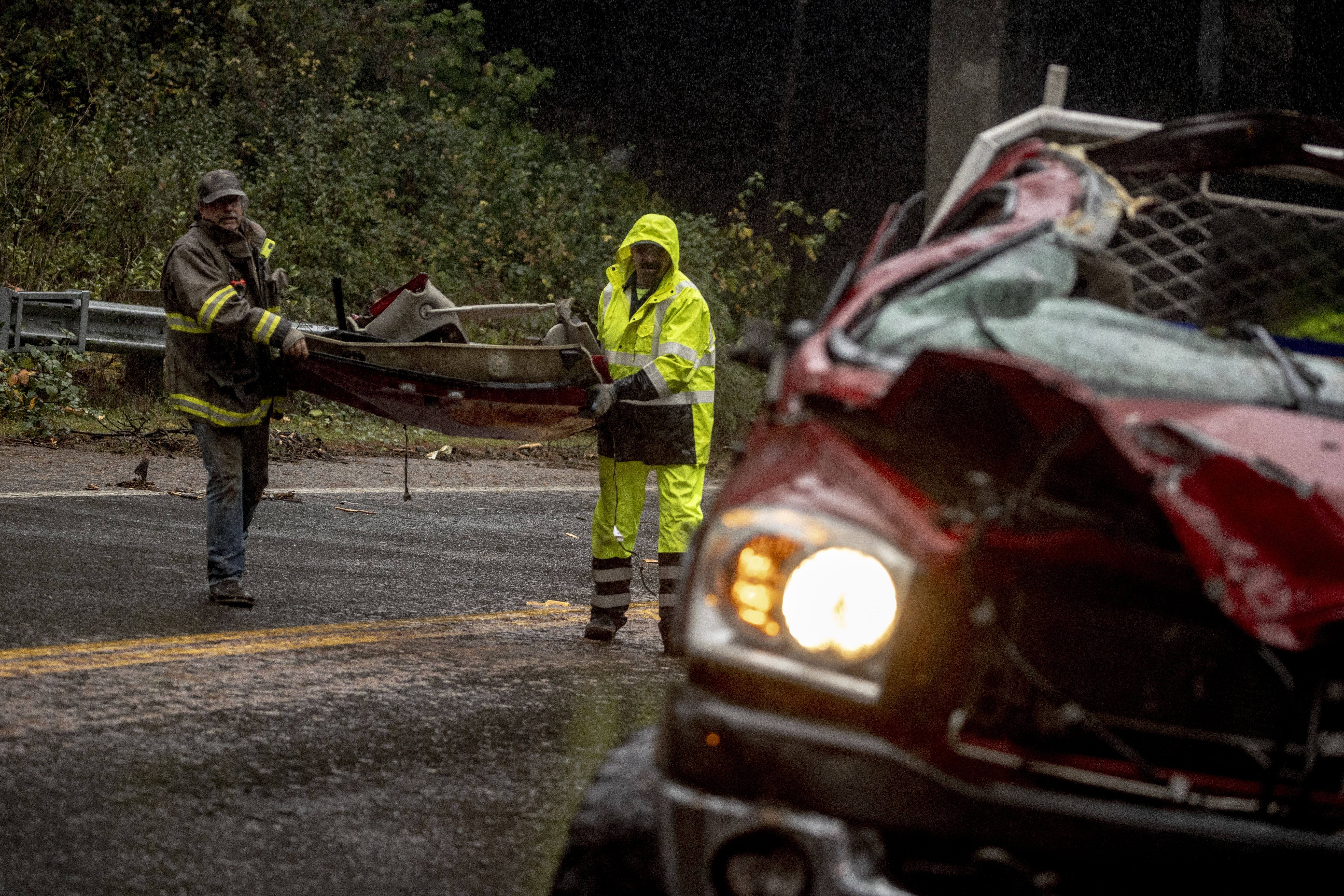 Workers remove vehicle debris at a collision between a downed tree and a vehicle amidst the ongoing atmospheric river event in Loleta, Calif., Wednesday, Nov. 20, 2024.