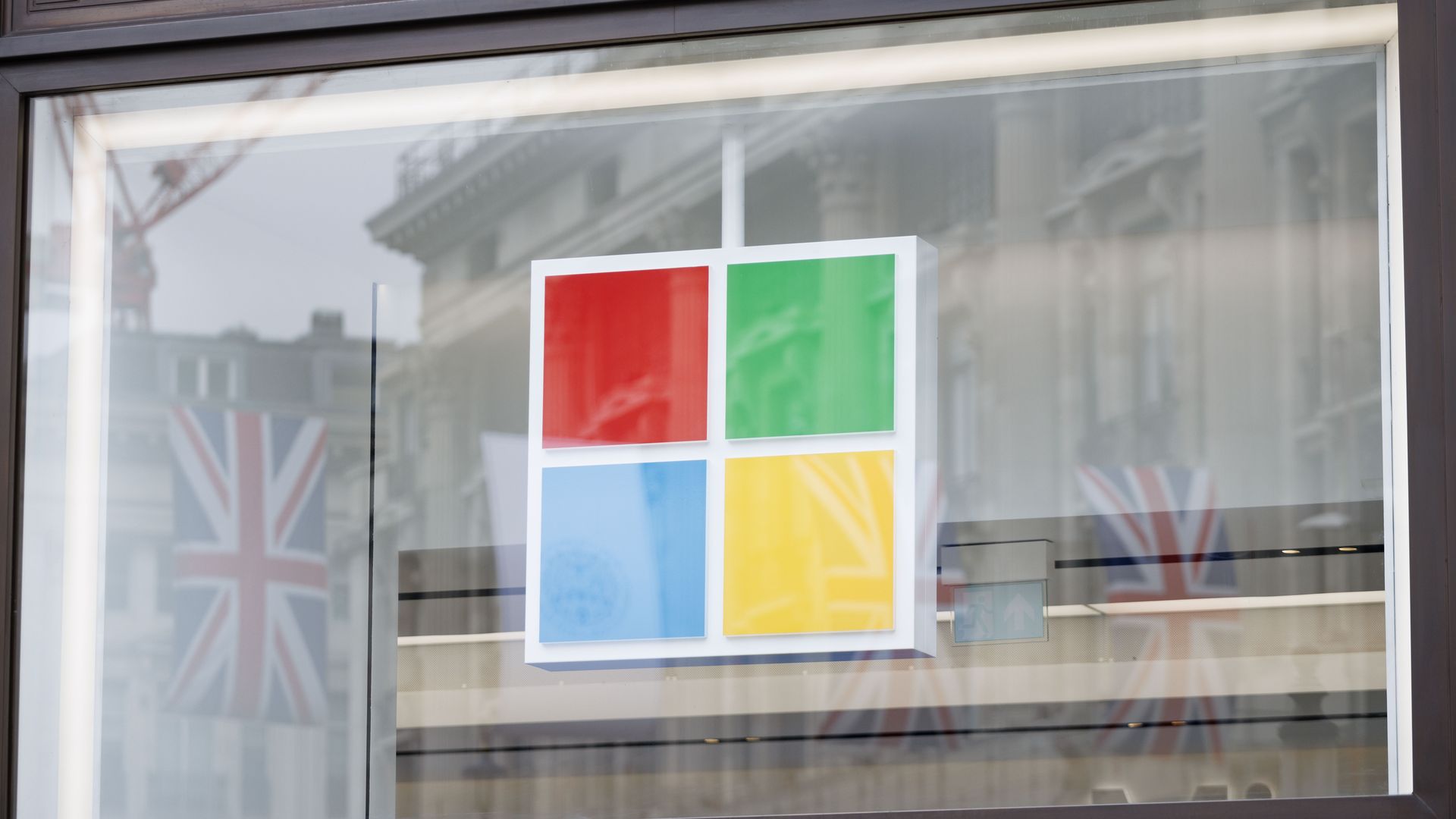 Photo of a Microsoft logo through a window with the British Union Jack visible in the window's reflection