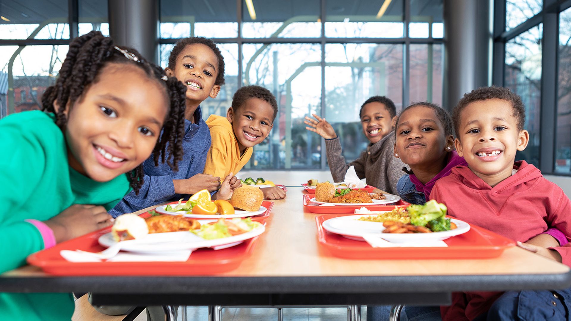 Six kids sit at a cafeteria lunch table 