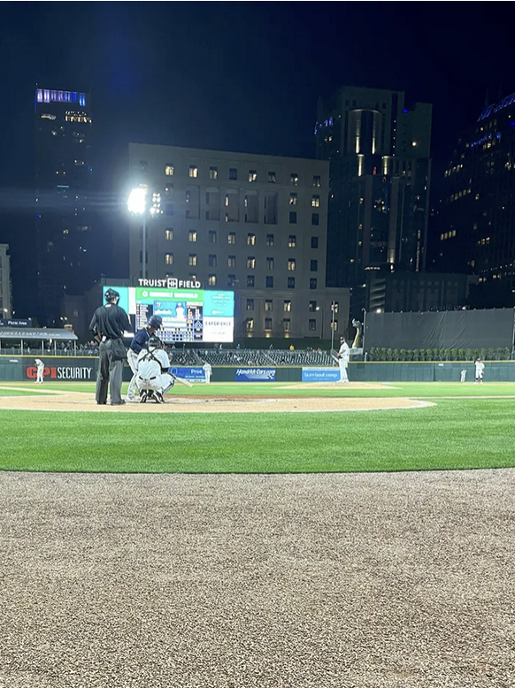 A pitcher standing on a pitching mound, about to throw to a batter and catcher. An ump is standing behind them.